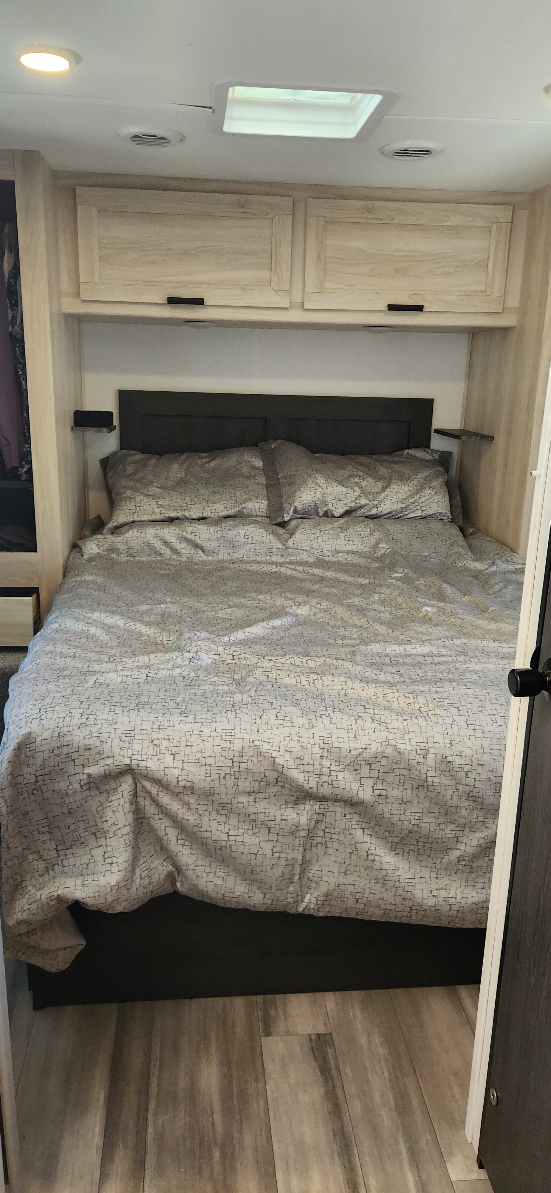 A cozy RV rental bedroom interior, featuring a bed with patterned duvet, overhead cabinets, and wood-look flooring.. Forest River Sunseeker LE 2024