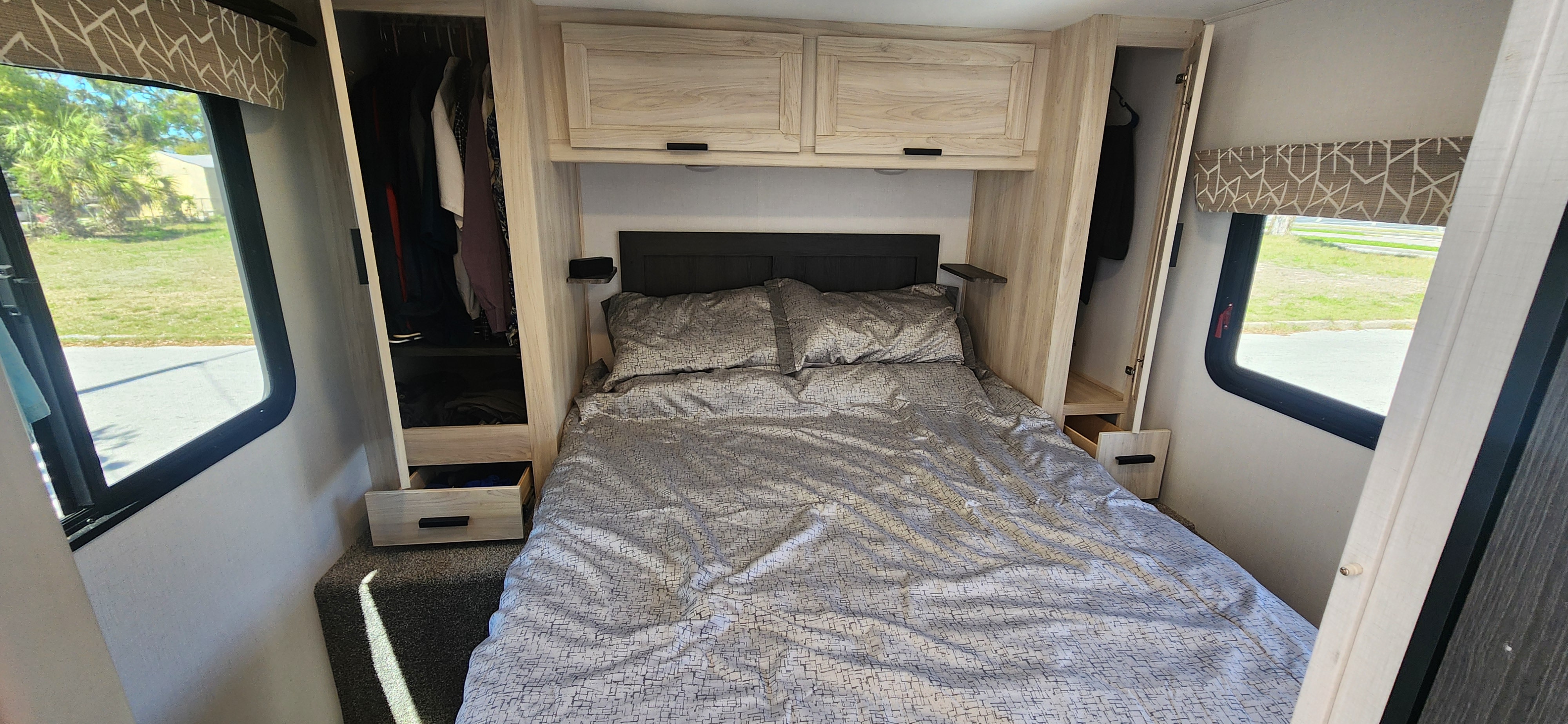 Bright RV rental bedroom: cozy bed, overhead storage, side closets, and large windows revealing the outdoors.. Forest River Sunseeker LE 2024