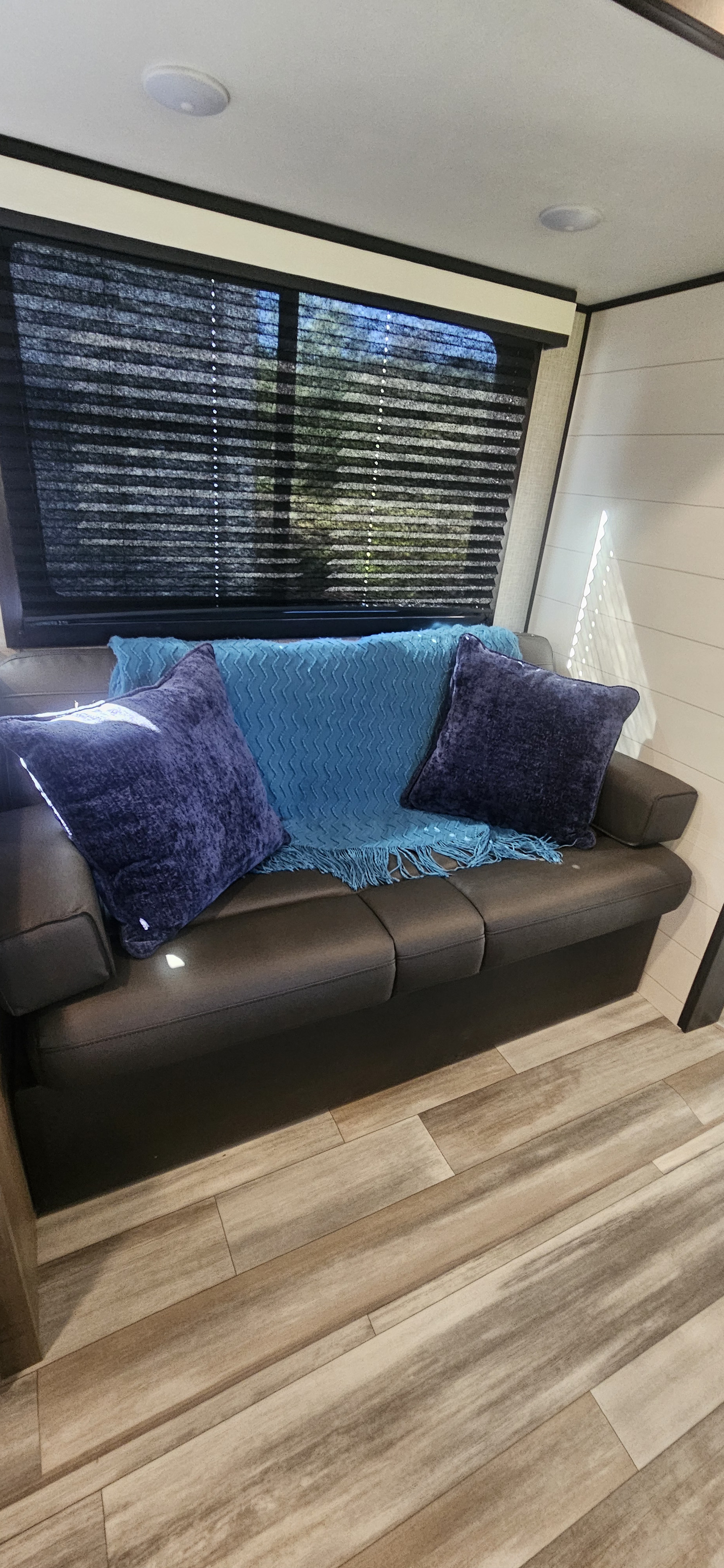 Cozy RV rental living space with dark sofa, blue blanket, and purple pillows. Window blinds visible, perfect for travel.. Jayco Jay Flight 267BHS 2024