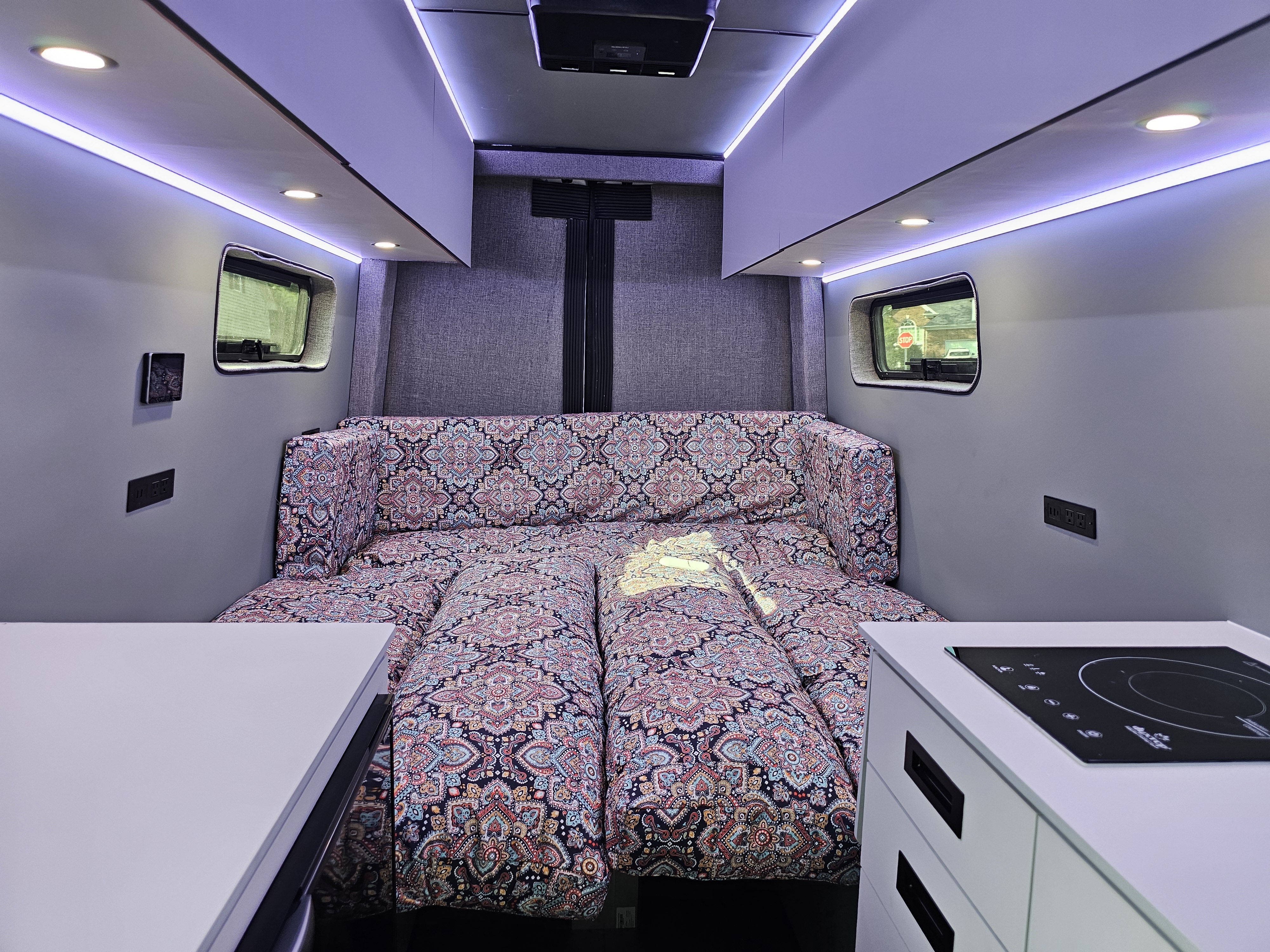 Cozy RV rental interior features a vibrant patterned bed, sleek induction cooktop, and bright LED strip lighting. Ideal for road trips.. Sovereign Vans Mercedes Benz Sprinter 2500 2022