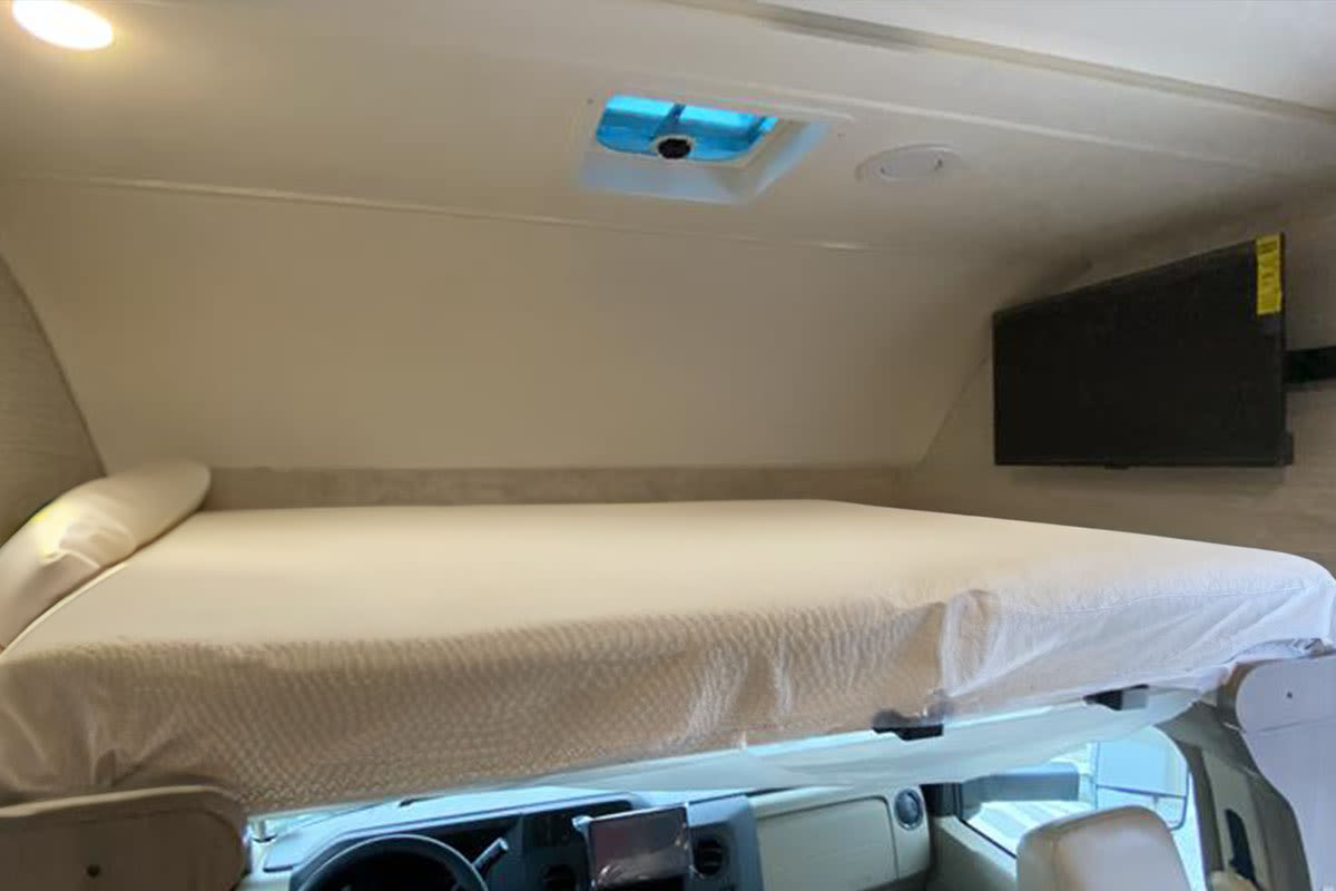 Cozy overhead bunk bed in an RV rental, complete with a TV and roof vent.. Winnebago Spirit 2023