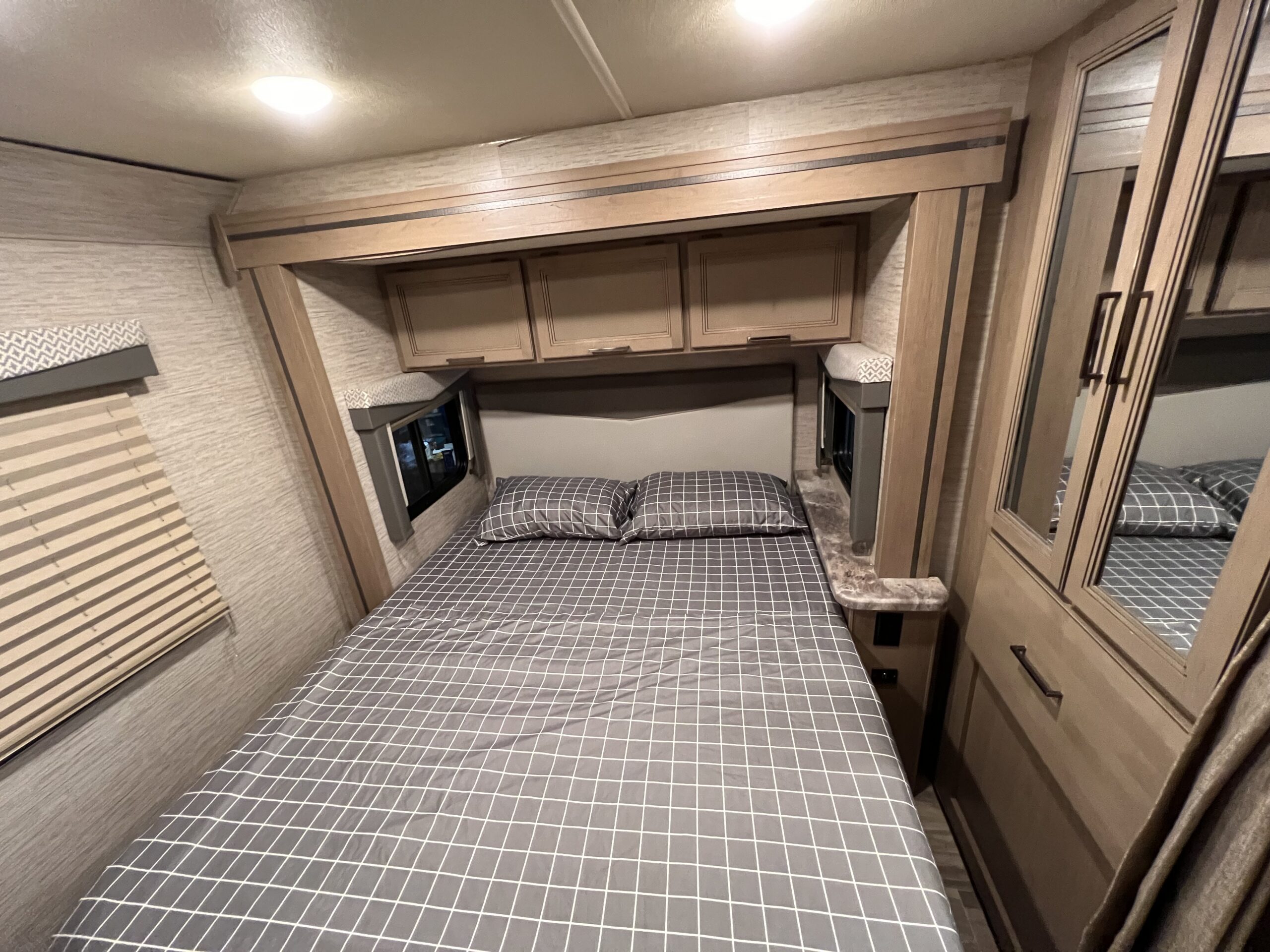Inside a comfortable RV rental bedroom featuring a checkered bed, overhead storage, and mirrored wardrobe for your travels.. Thor Motor Coach Four Winds 2022