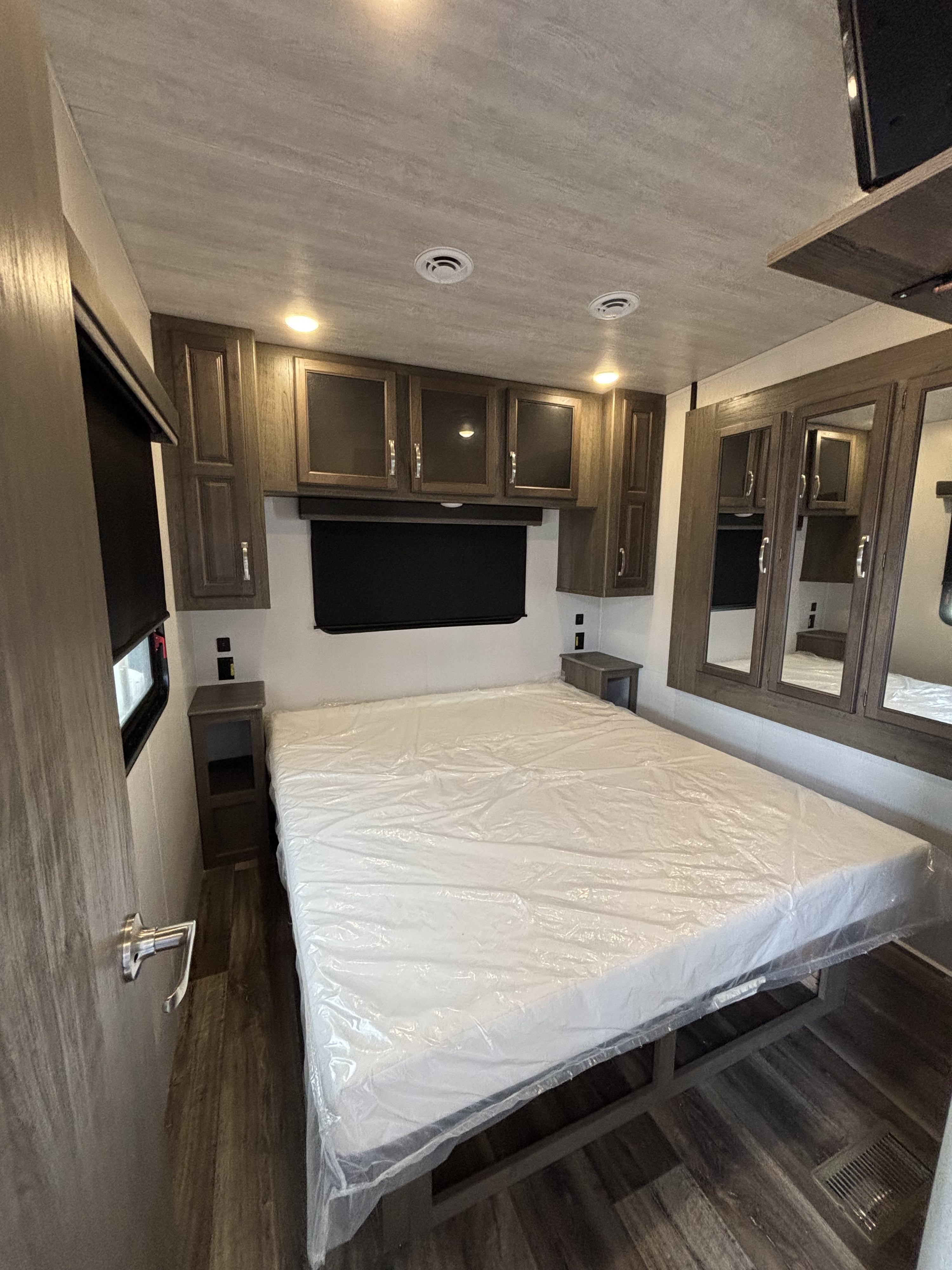 Inside an RV rental: a well-appointed bedroom with a plastic-covered bed, ample cabinets, and mirrored closet.. Keystone Cougar 2021