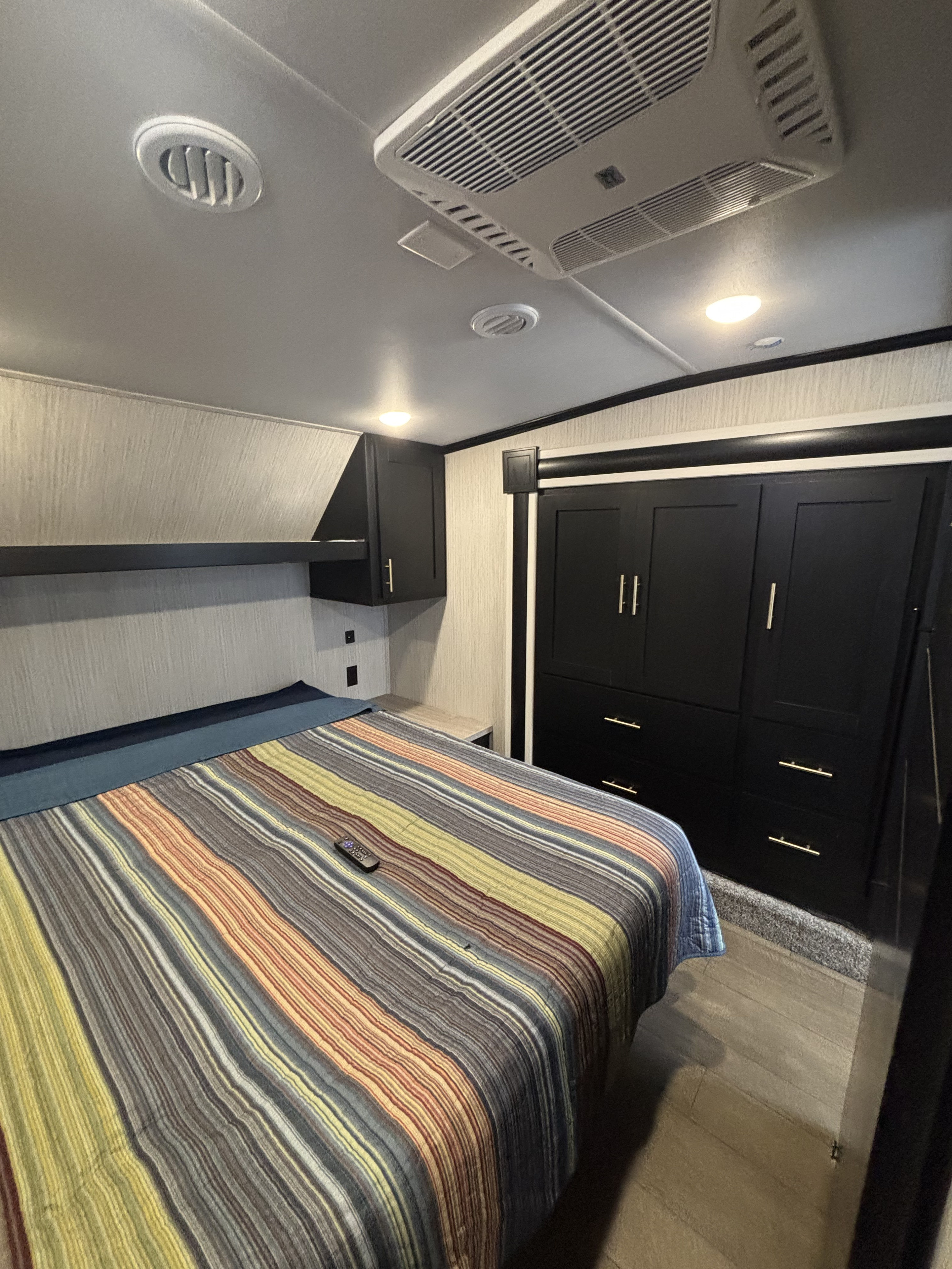 Experience comfort in this RV rental bedroom, featuring a cozy striped bed, ample storage, and modern amenities.. Forest River Wildcat 2021