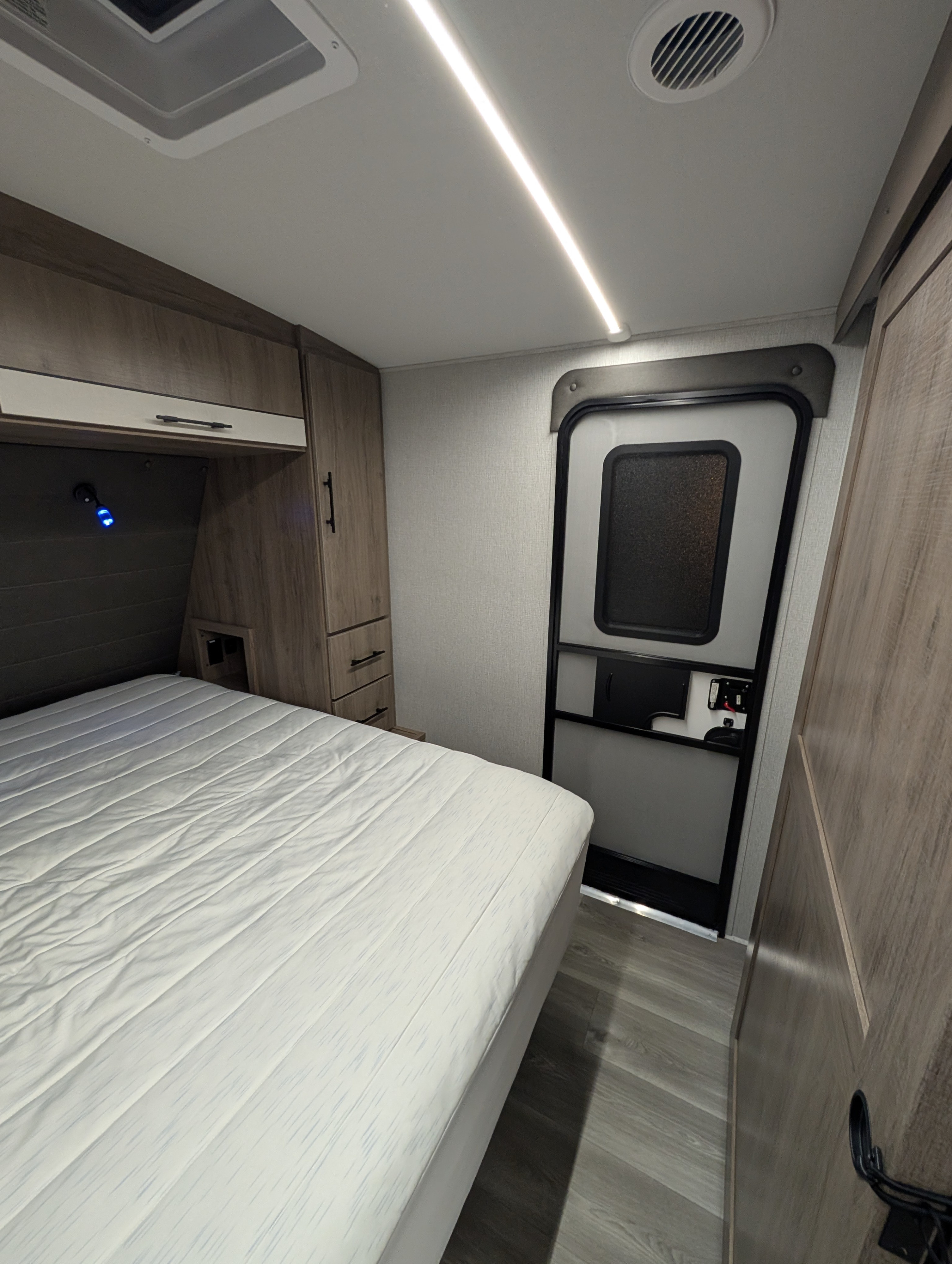 Cozy RV rental bedroom with white mattress, wood cabinets, entrance, ceiling light strip, and floor vent.. Grand Design Imagine 2024