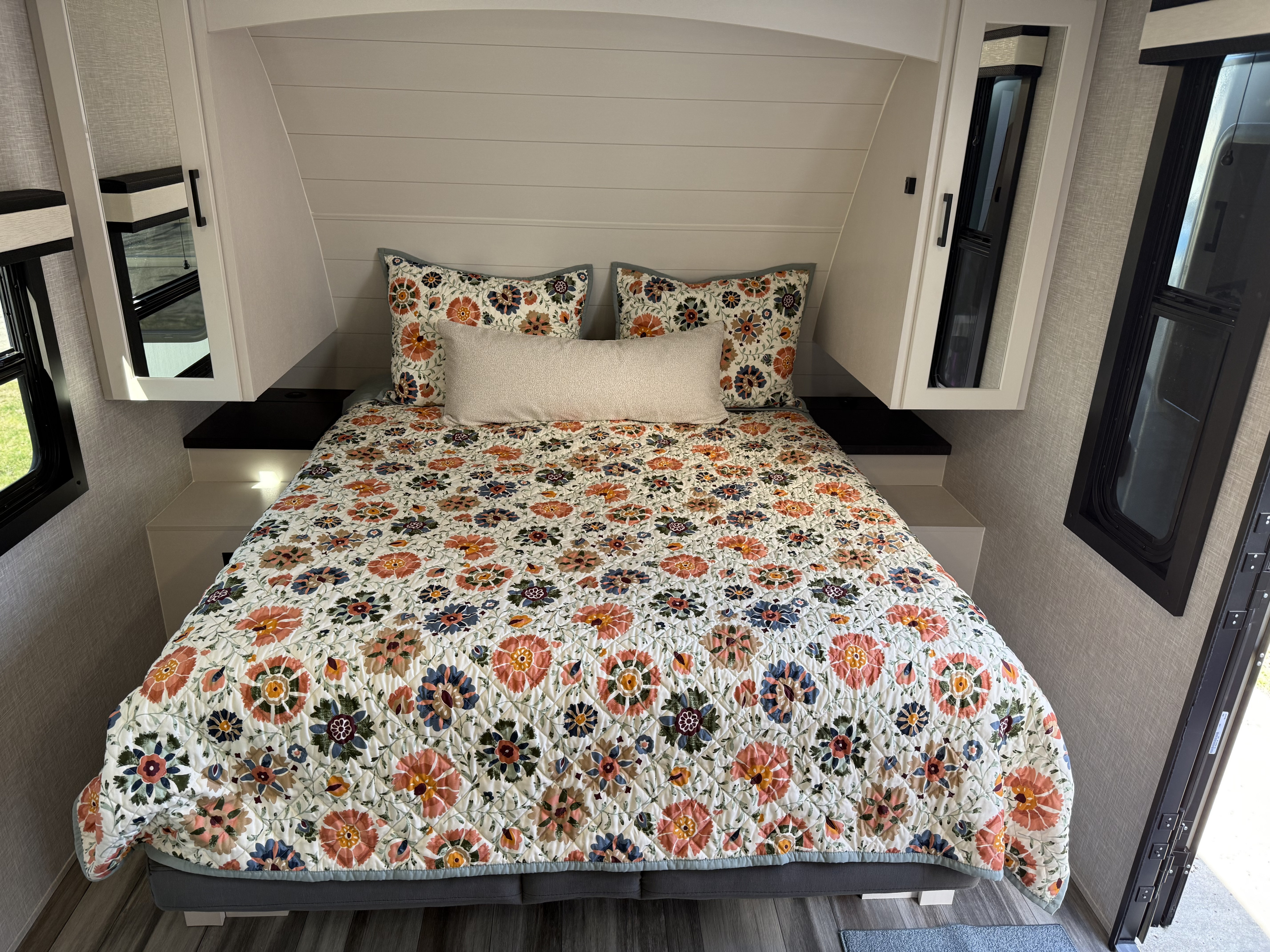 Cozy RV rental bedroom featuring a bed with a vibrant floral quilt, pillows, side cabinets, and windows. Perfect for travel.. Jayco Jay Feather 2025