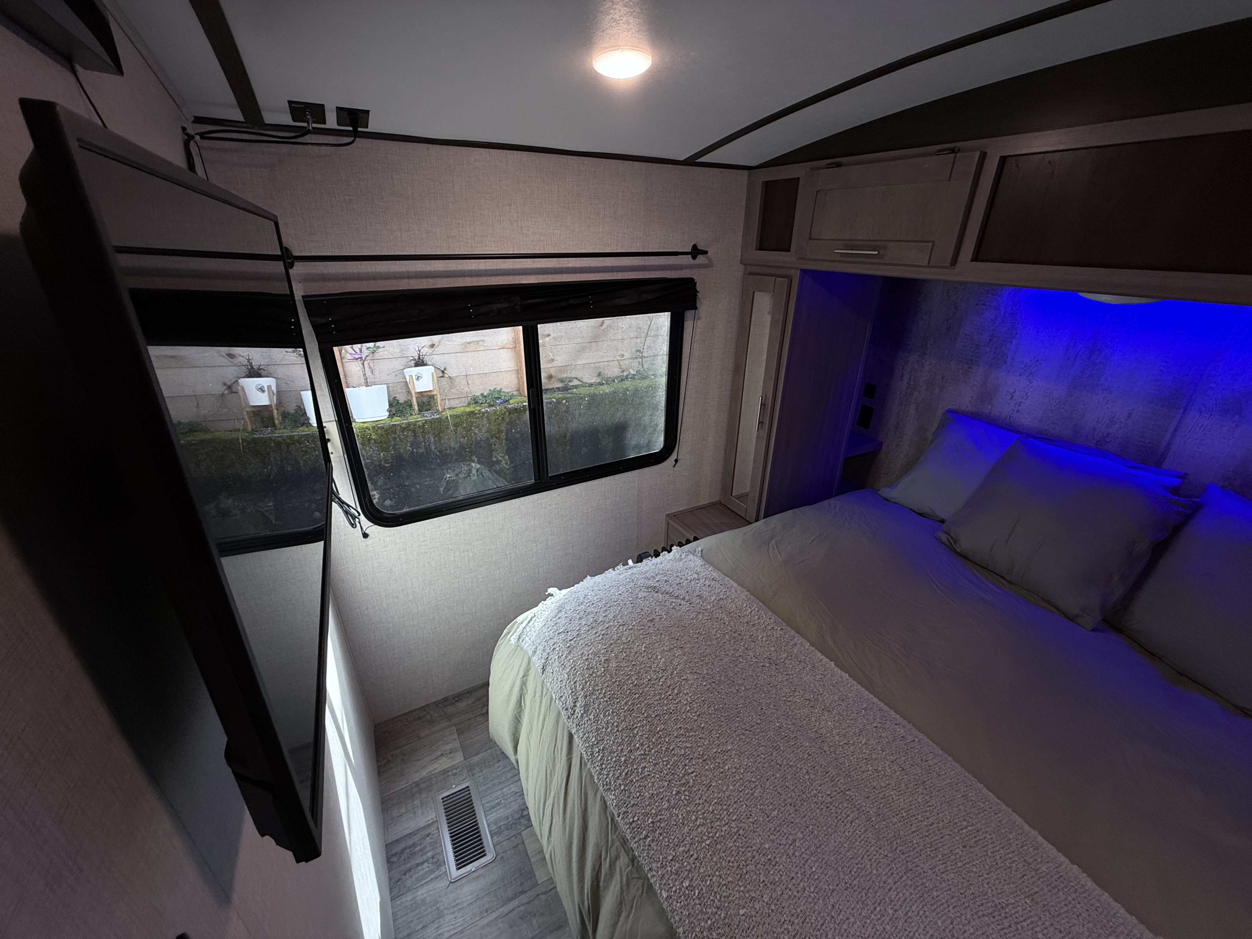 Cozy RV rental bedroom featuring a large bed, wall-mounted TV, and blue ambient lighting. View out window.. Crossroads Sunset Trail Super Lite 2021