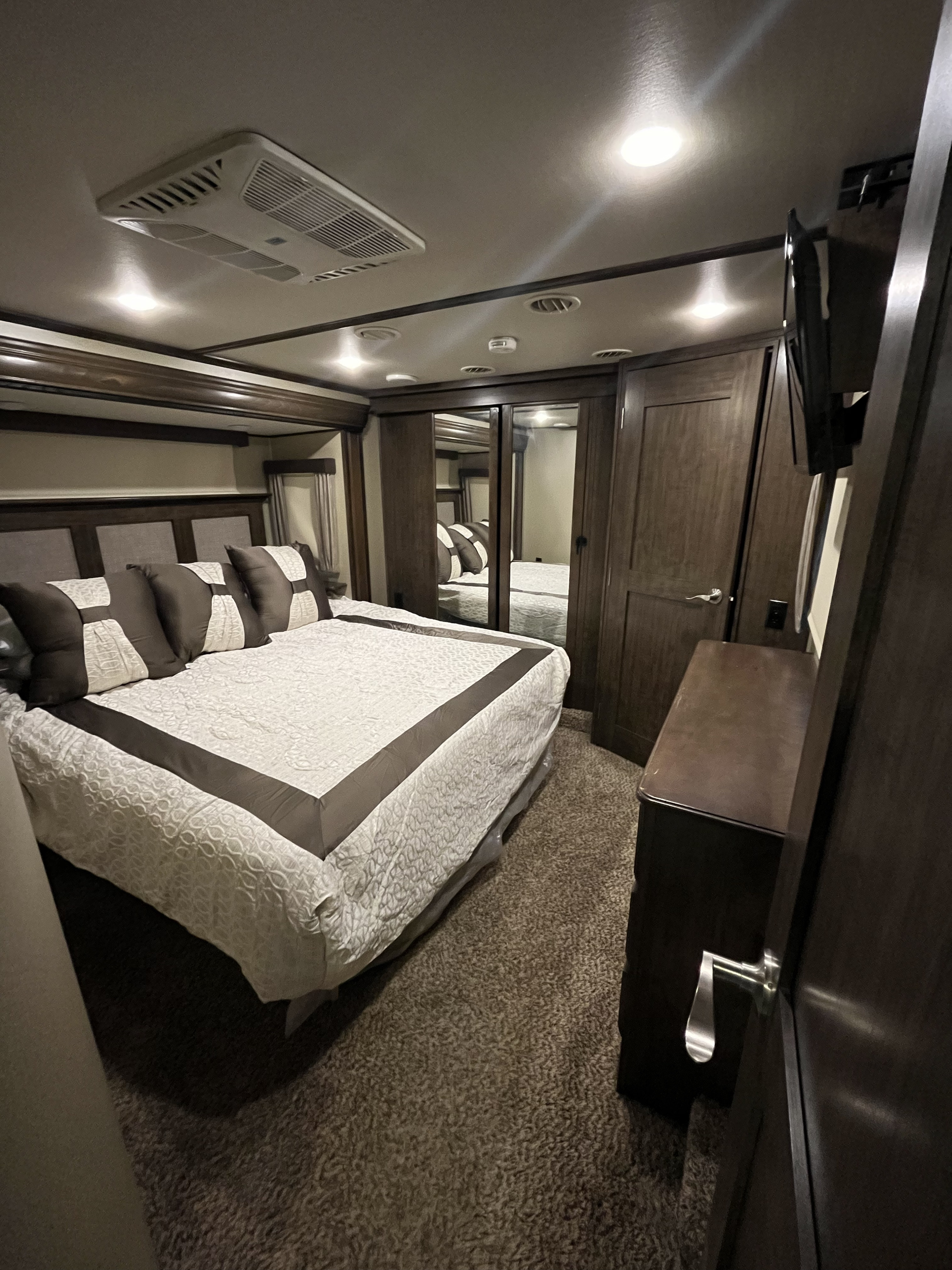 Step inside this modern RV rental bedroom, featuring a comfy bed, mounted TV, mirrored closet, and plush carpet.. Grand Design Solitude 375RES 2017