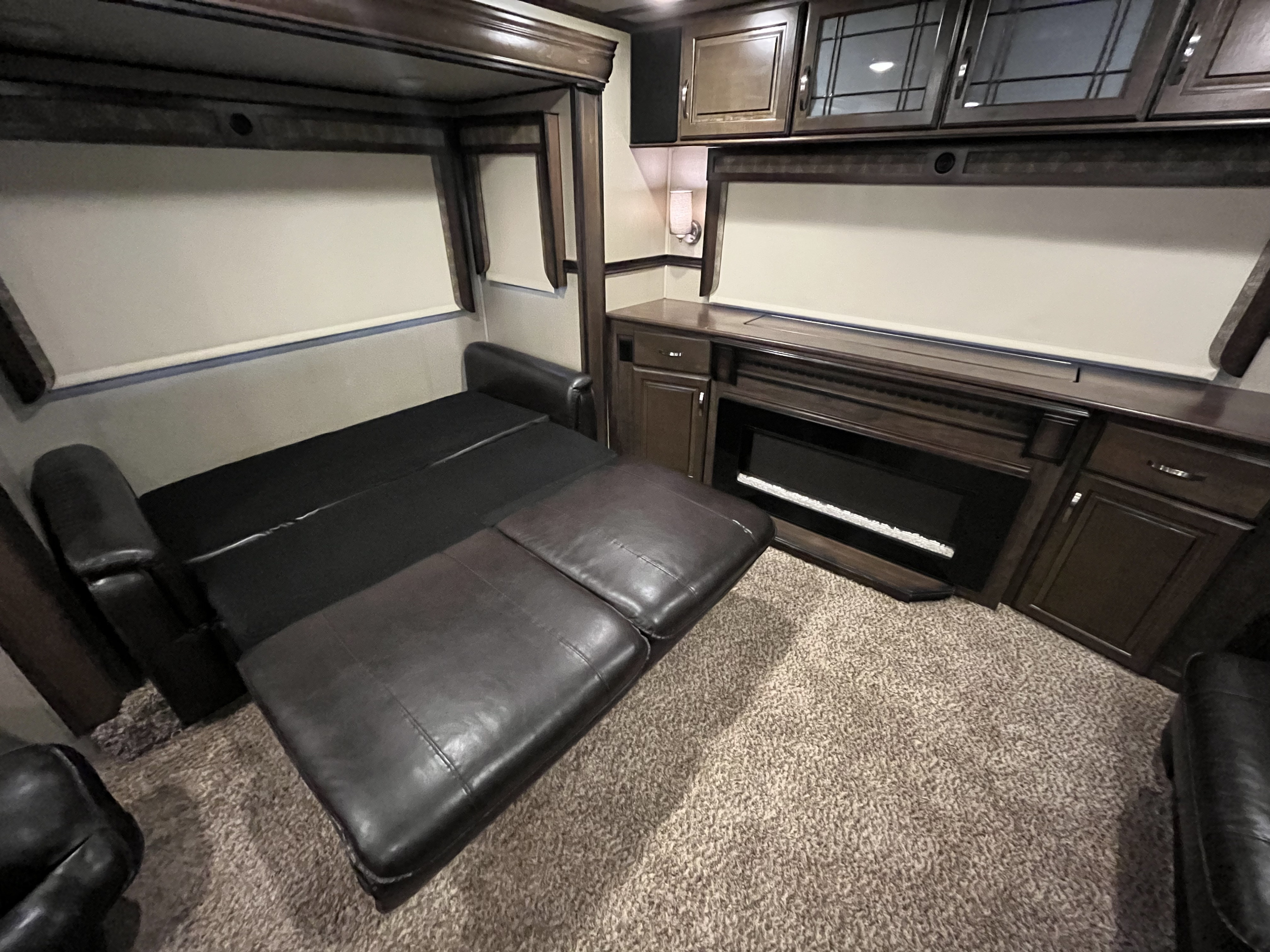 RV rental living area featuring a sofa converting to a bed, an electric fireplace, and dark wood cabinetry.. Grand Design Solitude 375RES 2017