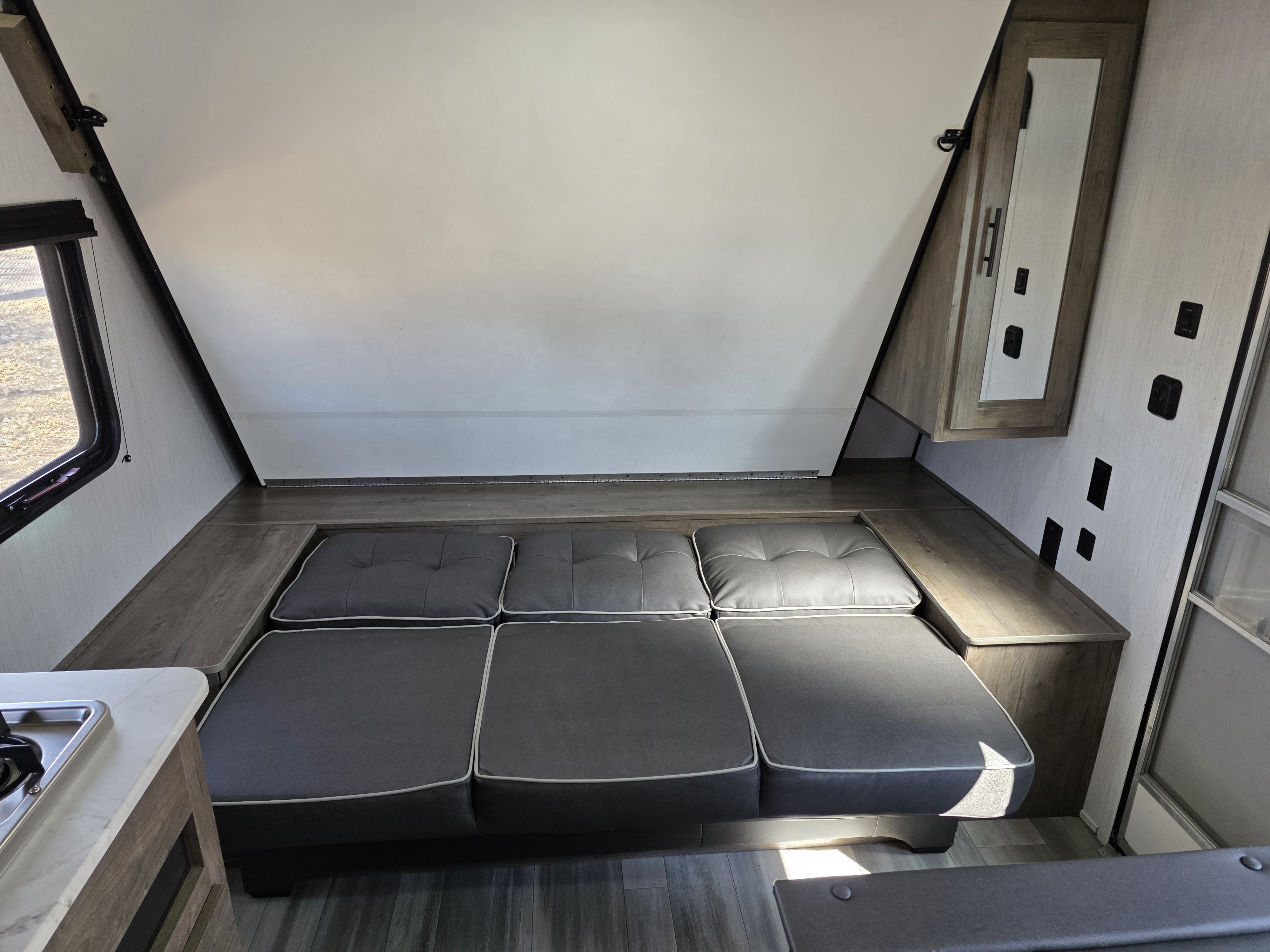 Inside an RV rental: a flexible interior with a convertible gray sofa bed beneath a sloping white ceiling, maximizing compact space.. Heartland RVs Pioneer Trail Blazer 2021