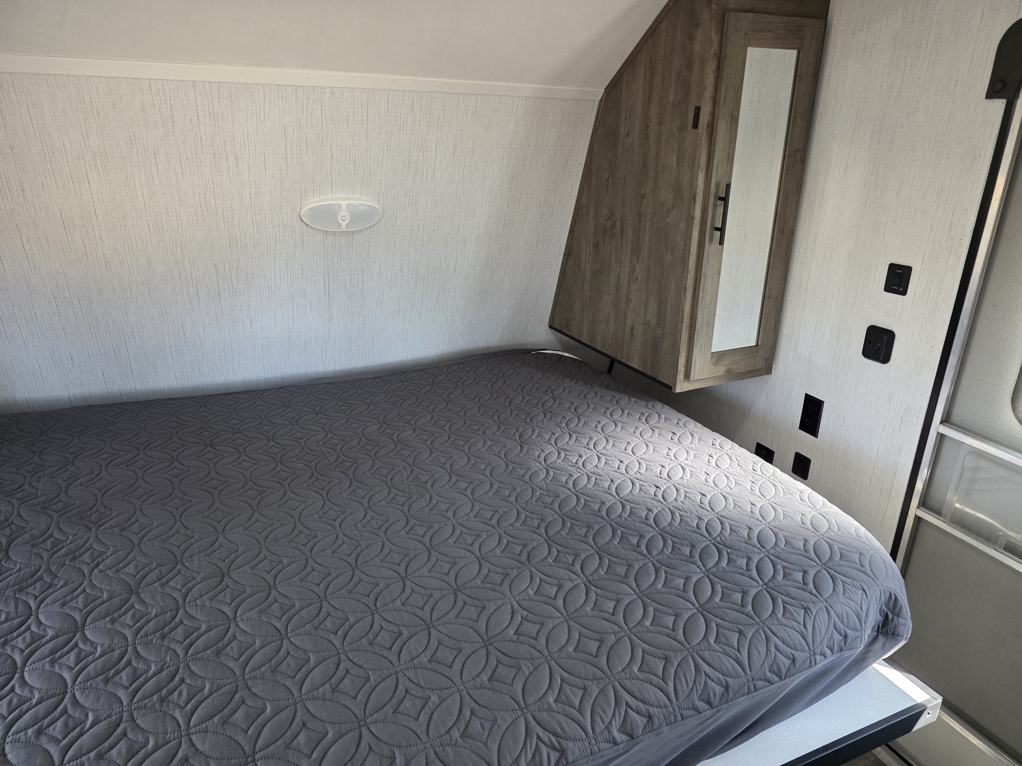 Comfortable RV rental bedroom featuring a grey patterned bed, simple wall light, and corner cabinet with mirror.. Heartland RVs Pioneer Trail Blazer 2021