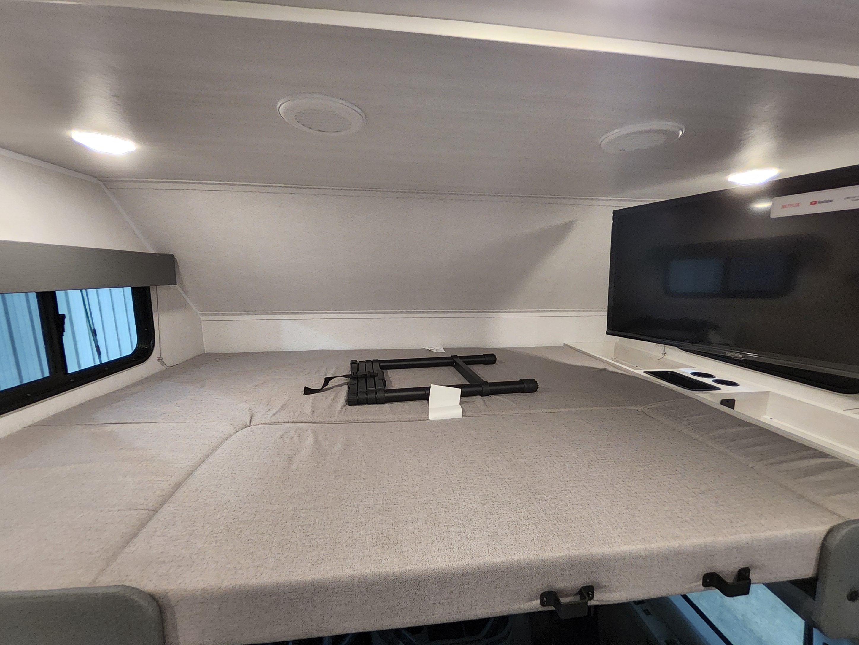 RV rental overhead bunk bed: a comfortable sleeping area with mattress, TV, window, and a folded ladder.. East To West Entrada 2000NS 2025