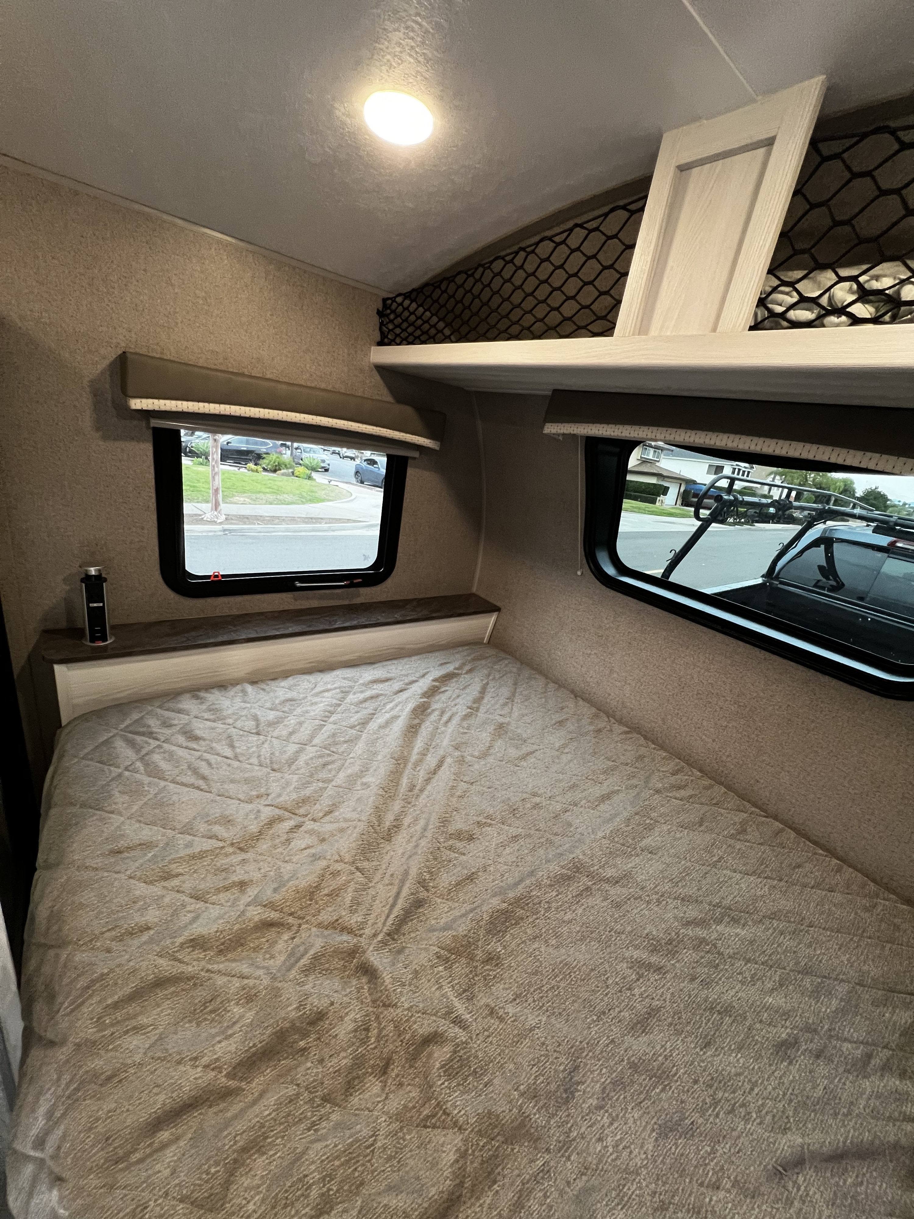 Cozy RV rental bedroom featuring a bed, pop-up outlet, two windows, and overhead storage nets.. Forest River Rockwood Geo Pro 2021