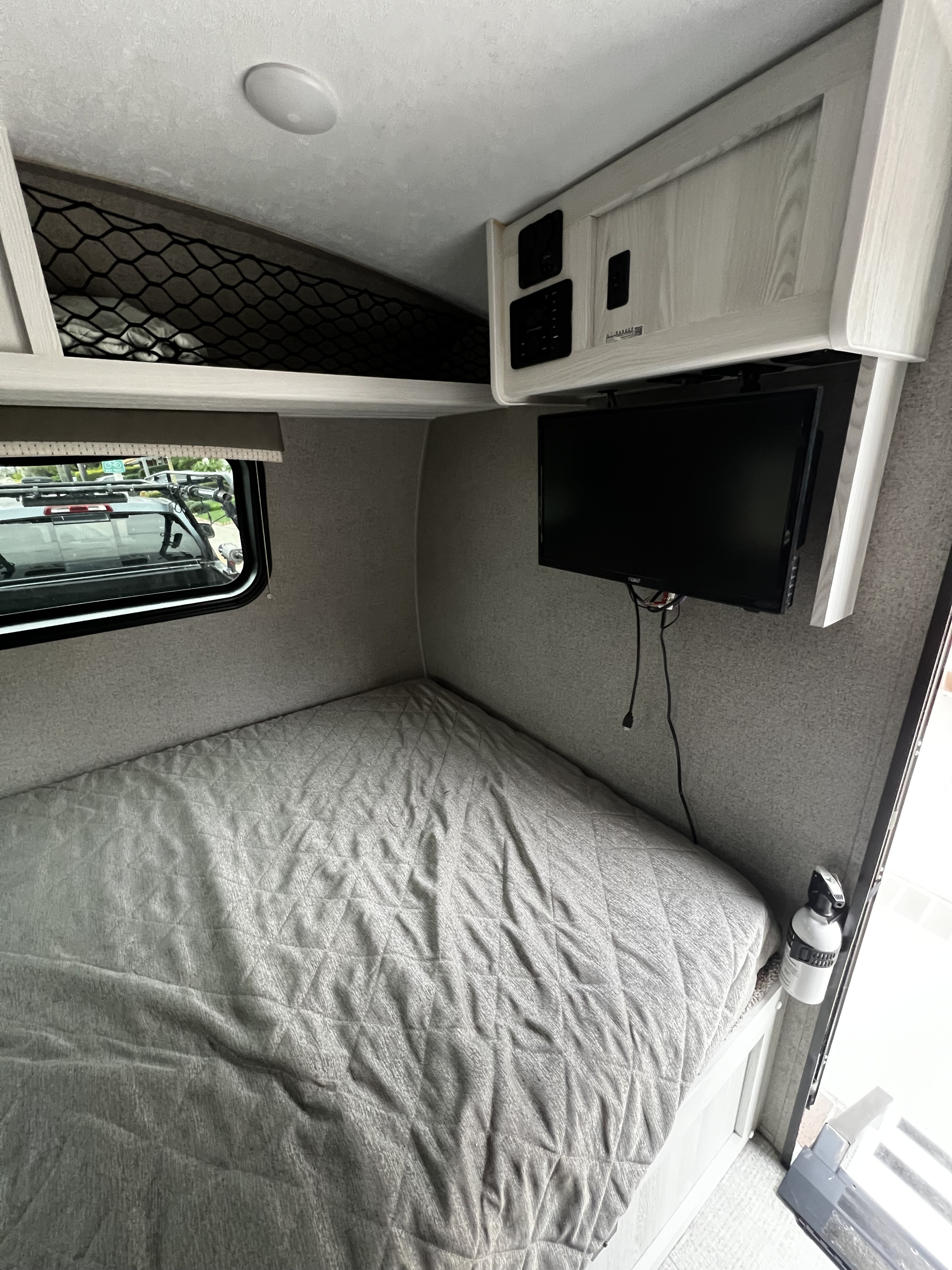 Explore this RV rental's bedroom: a quilted bed, wall-mounted TV, control panel, storage, and a window view.. Forest River Rockwood Geo Pro 2021