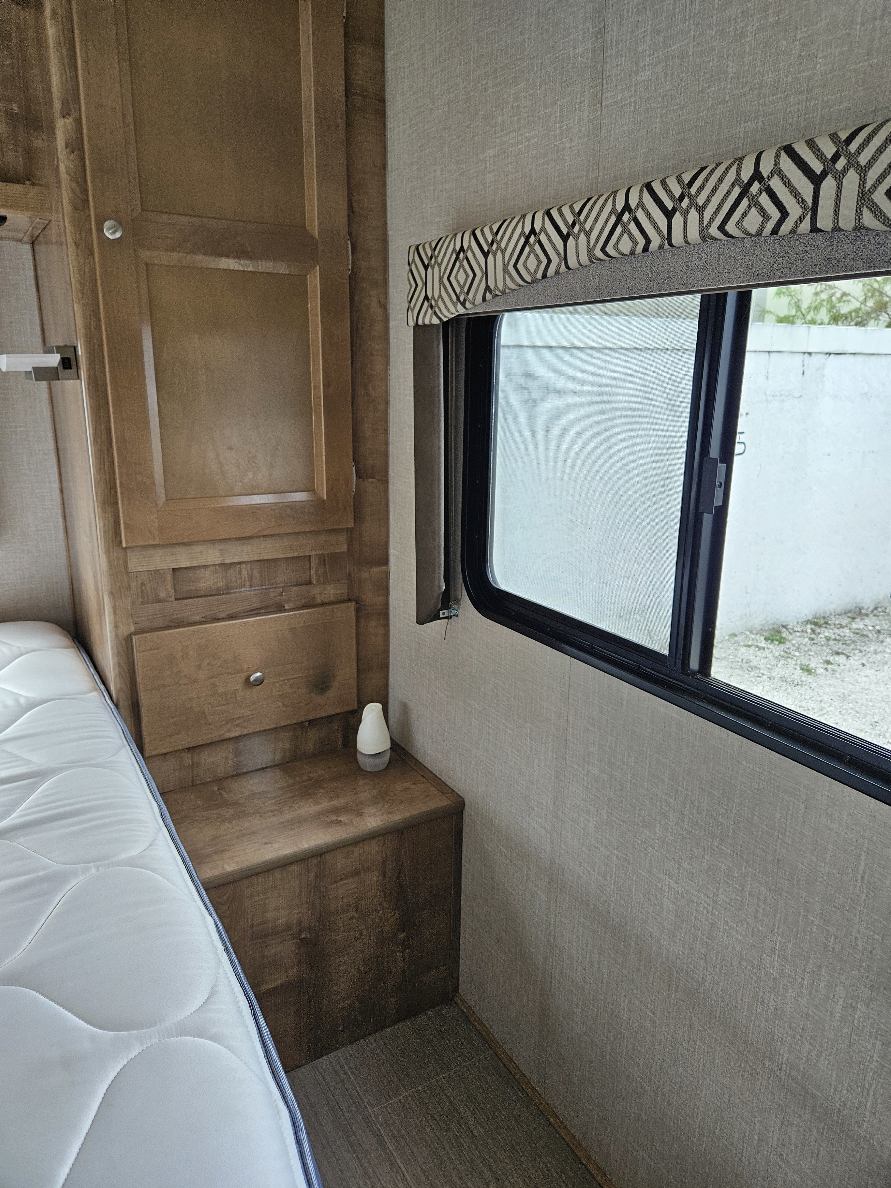 Experience comfort in this RV rental bedroom: bed, built-in wood cabinets, and window with stylish valance.. Forest River Coachmen Leprechaun 2019