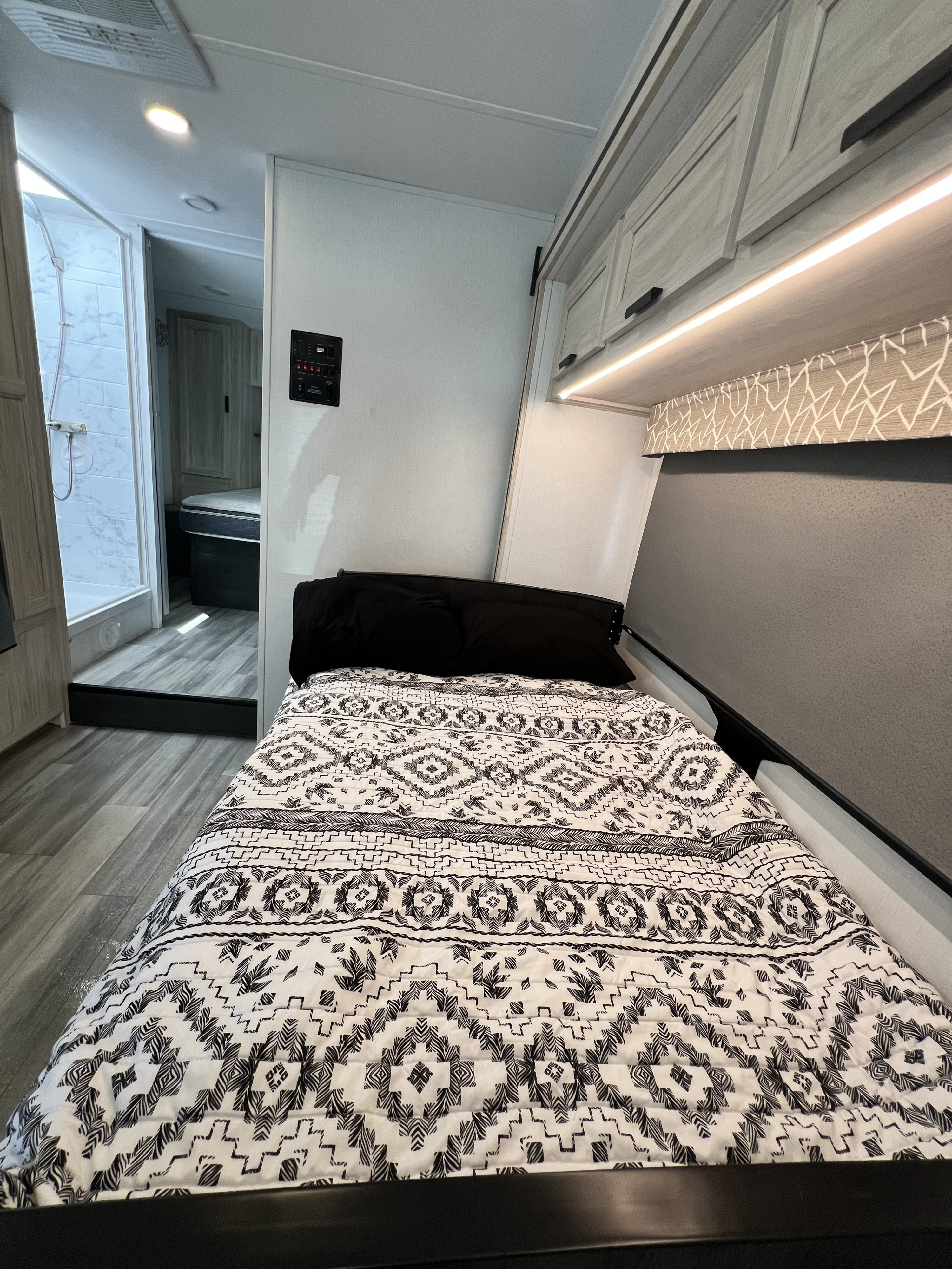 Cozy RV rental interior featuring a bed, overhead cabinets, under-cabinet lighting, and a view into the shower area.. Forest River Sunseeker 2024