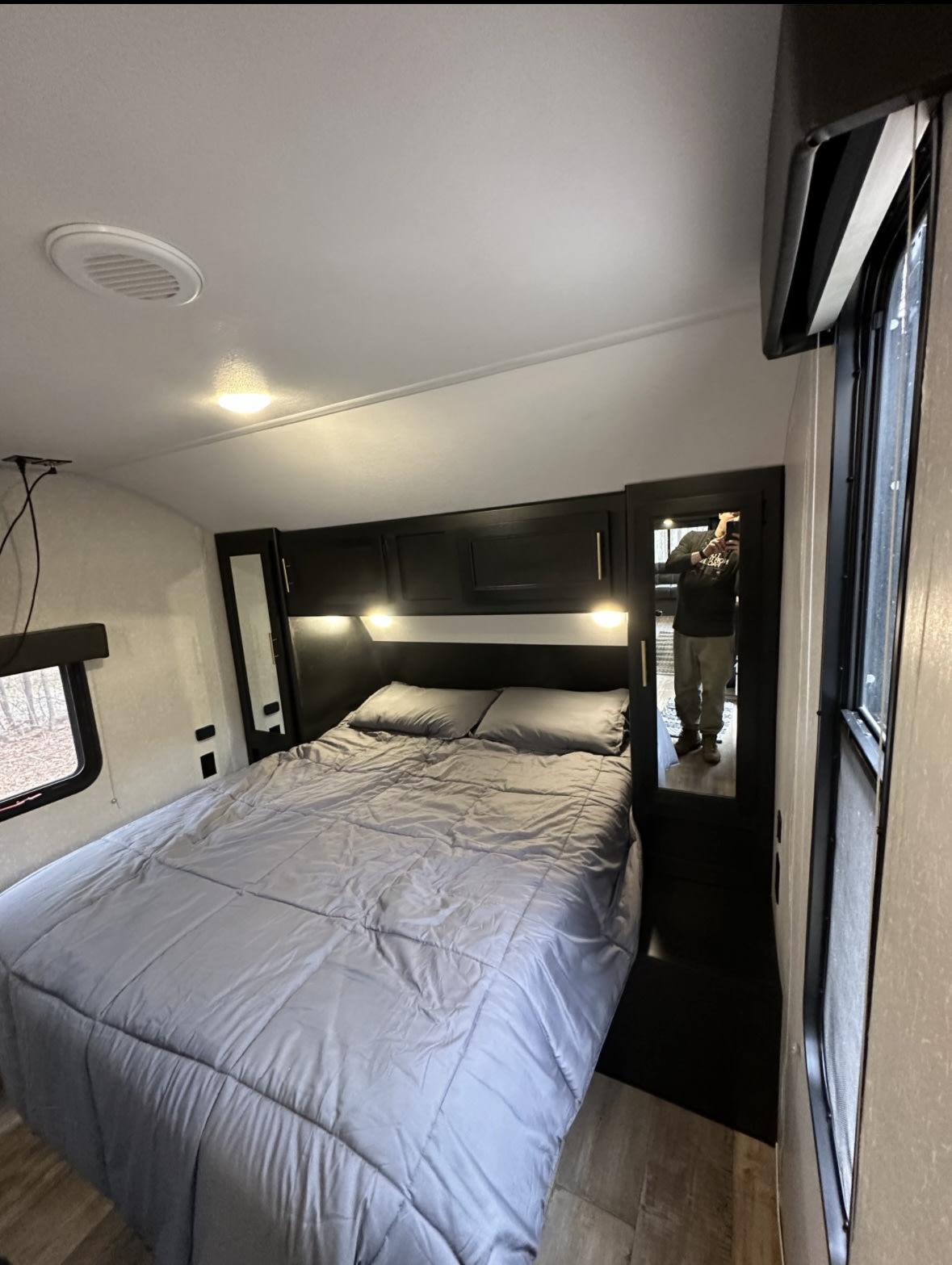 Spacious RV rental bedroom with a comfortable gray bed, overhead cabinets, and bright lighting. Includes a full-length mirror.. Forest River Cherokee 2022