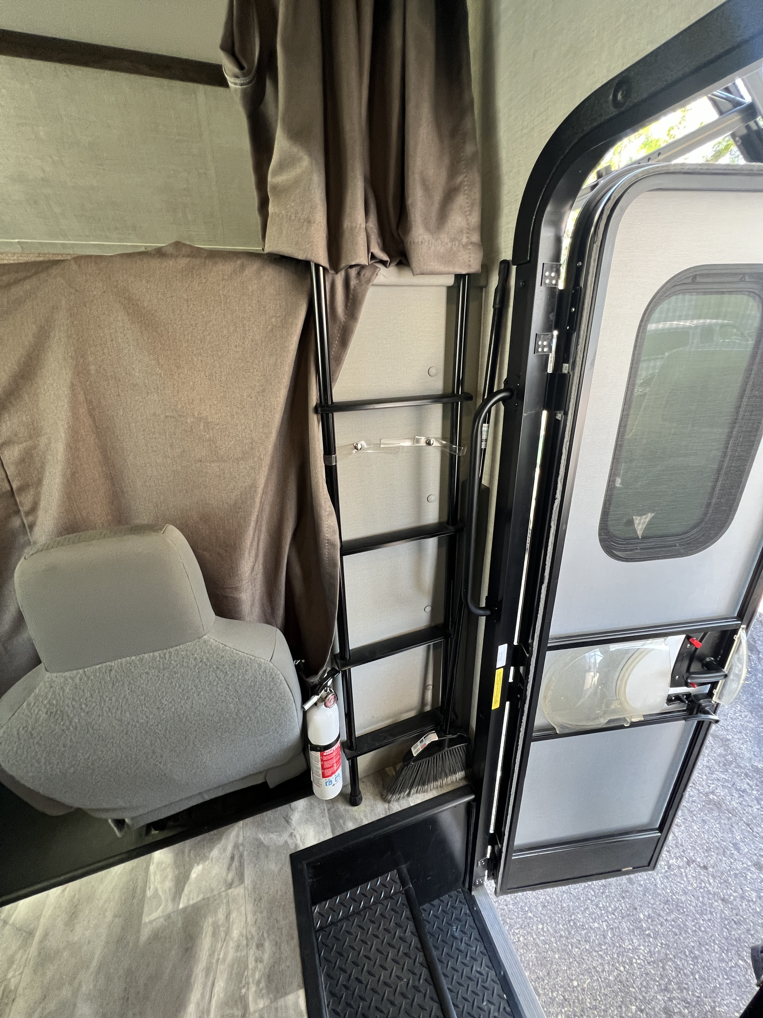 RV rental interior: the entrance area with an open door, a ladder, fire extinguisher, broom, and gray seat.. Gulf Stream Conquest 2023