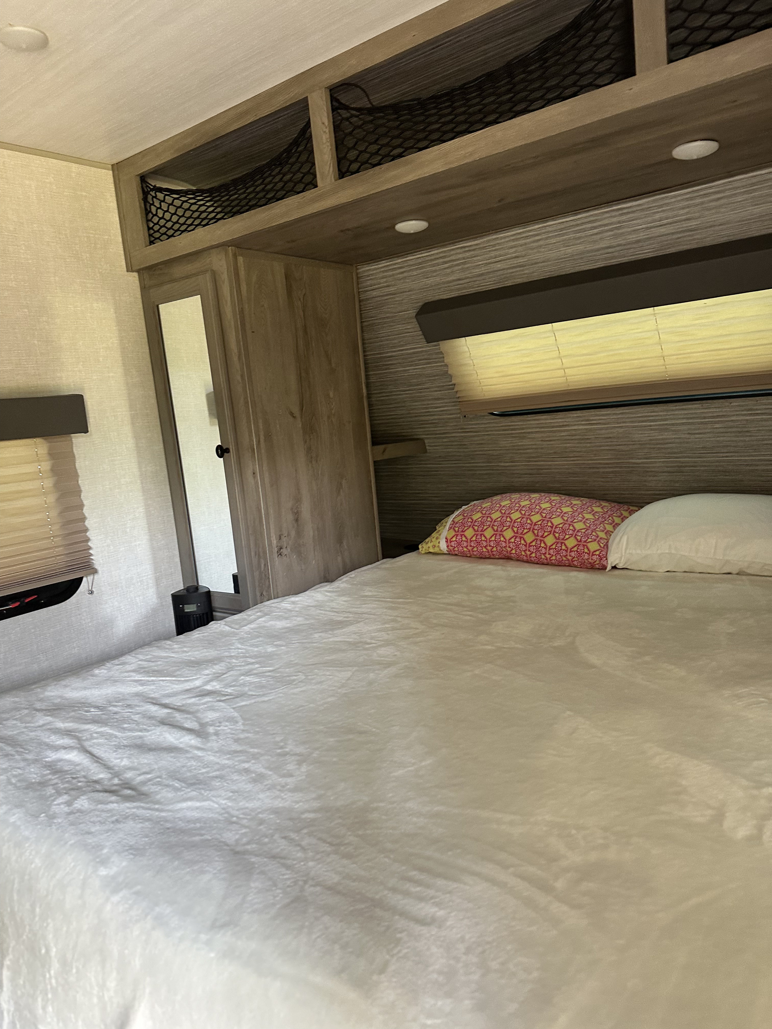Cozy RV rental bedroom with a comfy bed, patterned and white pillows, overhead storage nets, and window blinds.. Keystone RV Springdale 2020