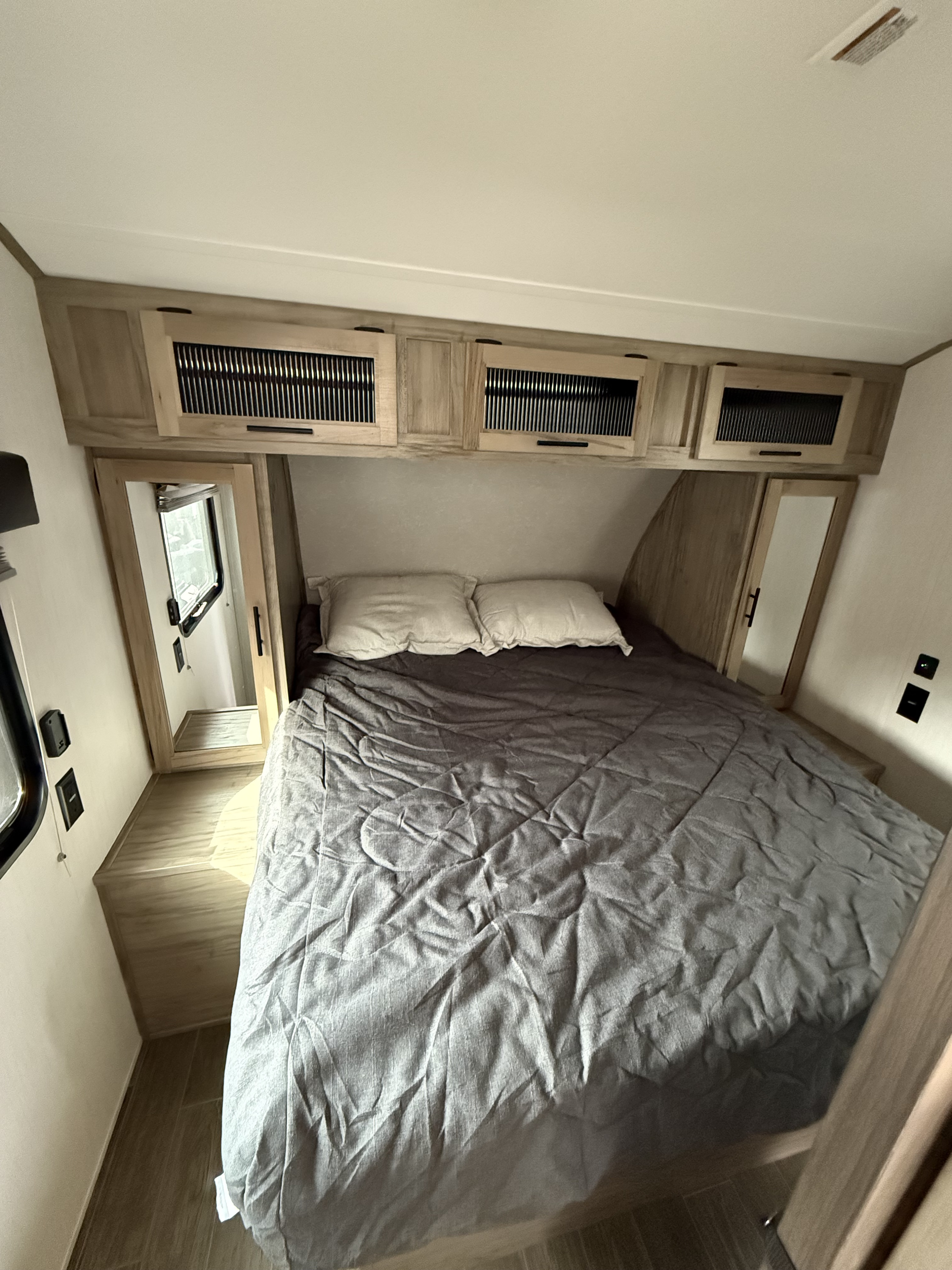 Cozy RV rental bedroom with grey bedding, ample overhead storage, and a large window. Ideal for compact living.. Forest River Cherokee Alpha Wolf 2022