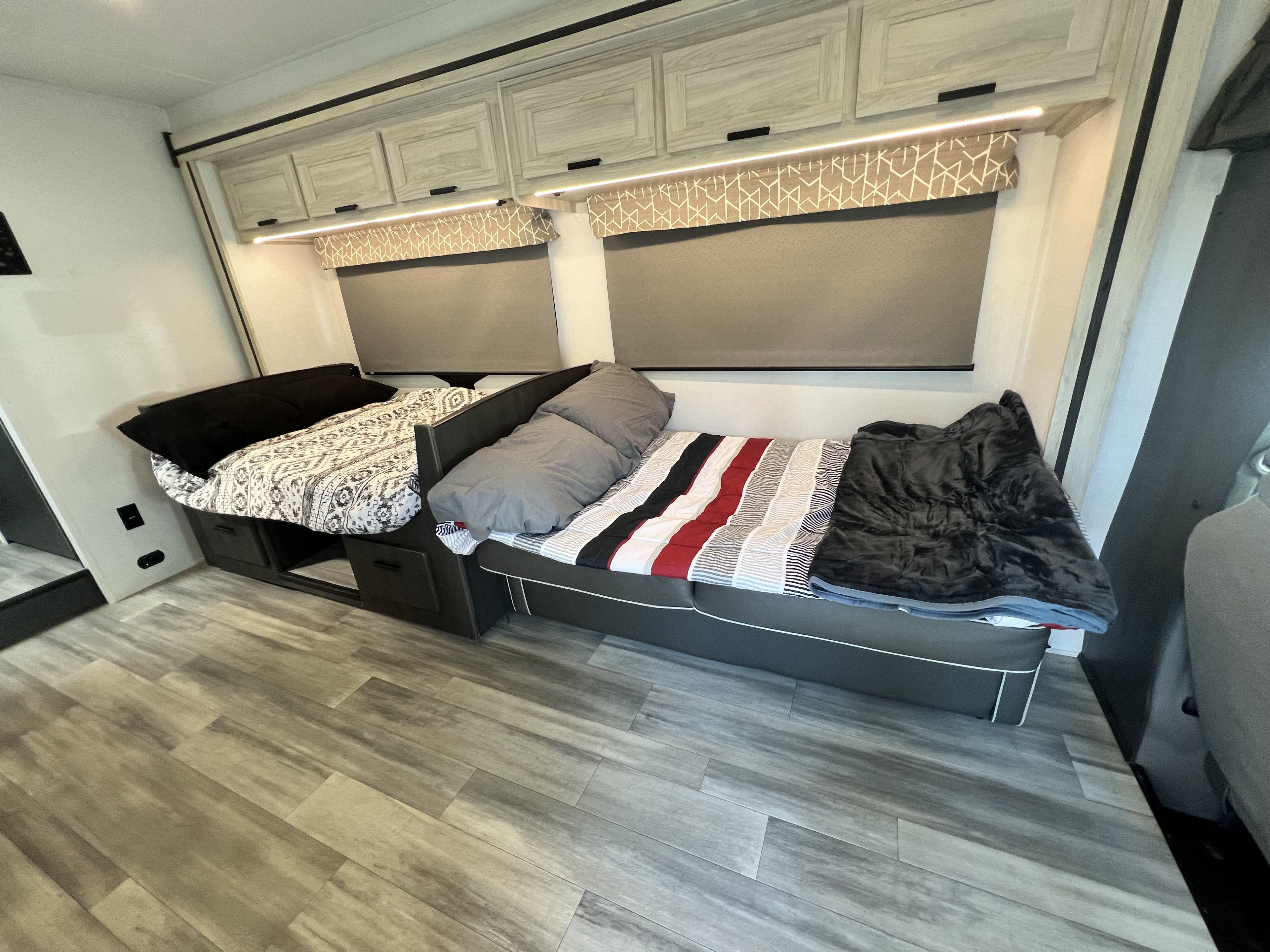 RV rental shows two modern sleeping areas with striped and patterned bedding, storage, and overhead cabinets.. Forest River Sunseeker 2024