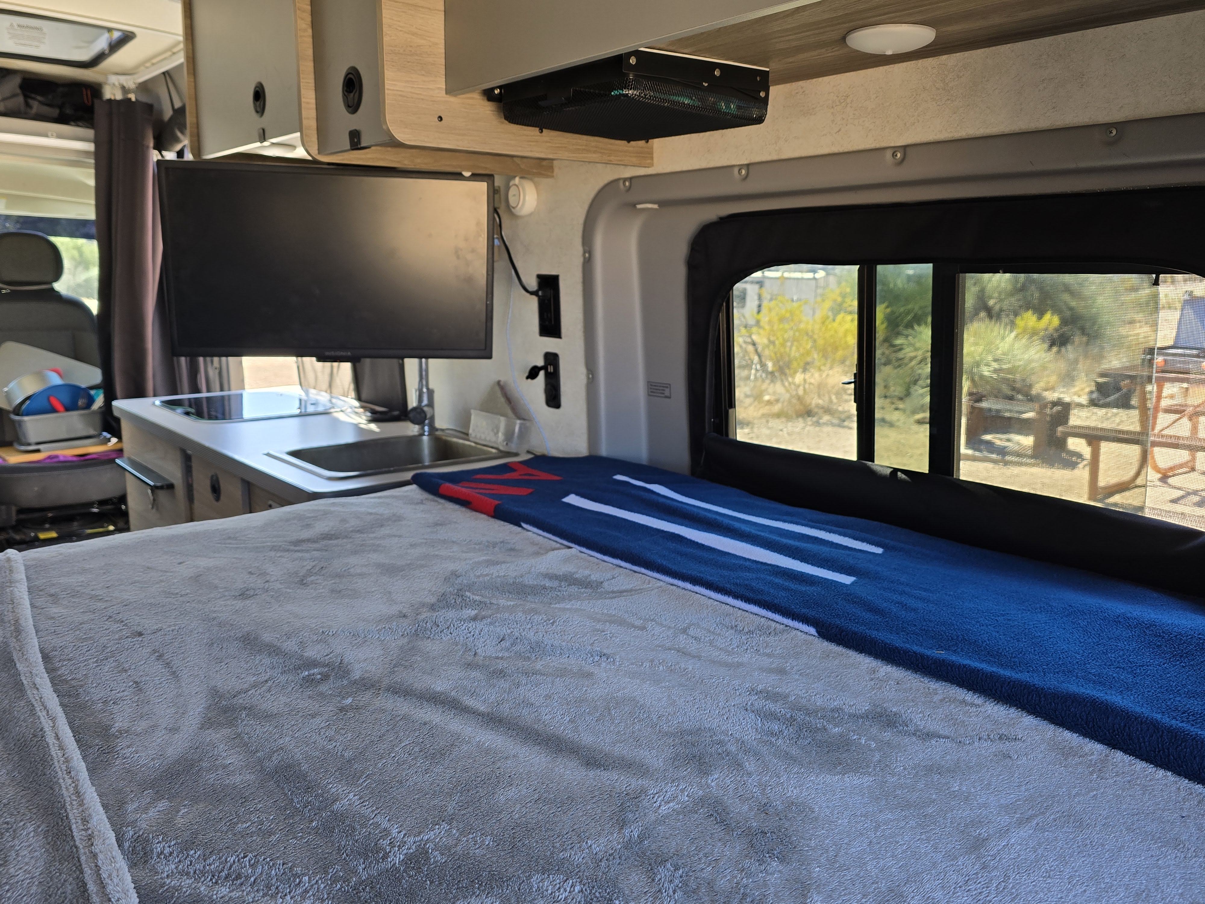 Inside an RV rental: a compact living space with a comfy bed, kitchenette, TV, and window view. Ready for travel!. Winnebago Solis 2023