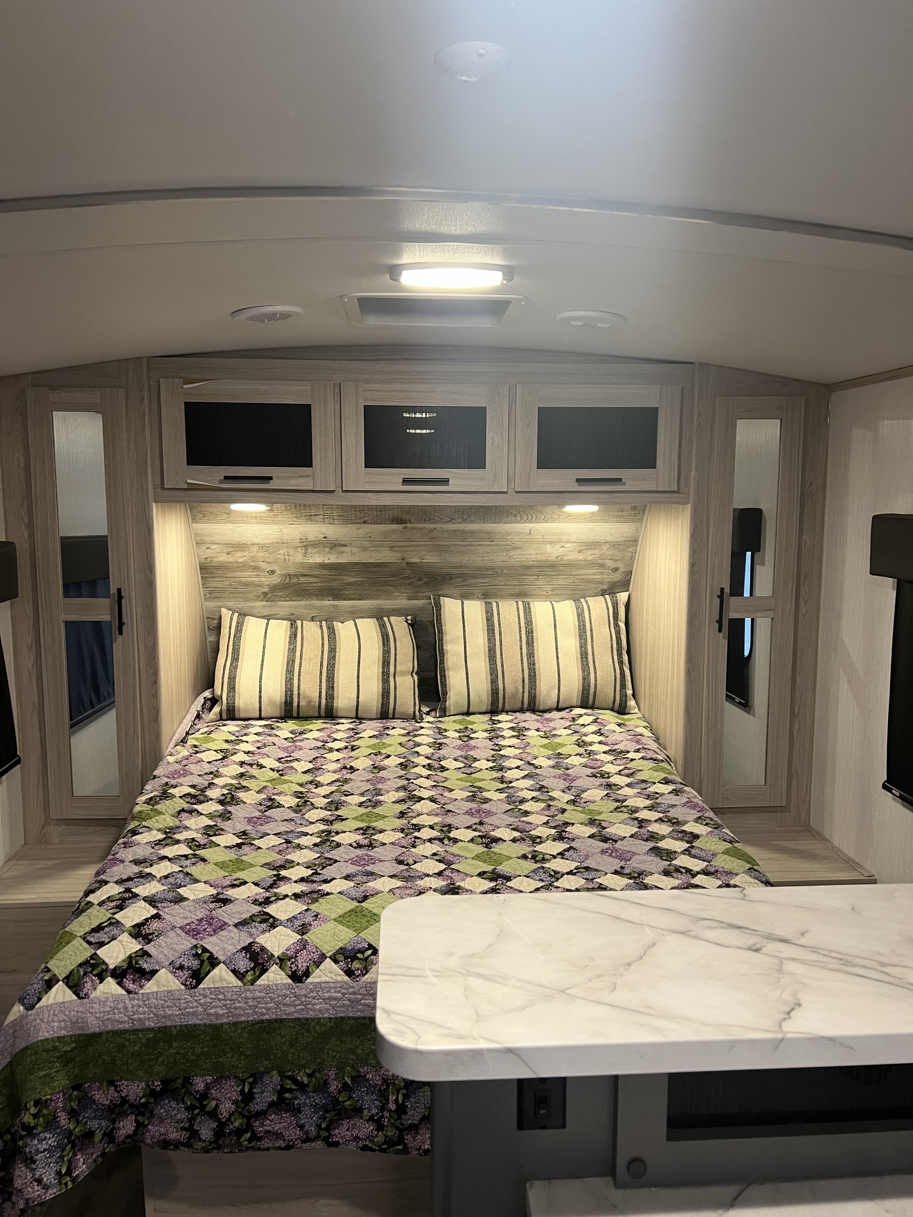 This RV rental bedroom features a vibrant quilt, striped pillows, light wood cabinets, and integrated lighting for cozy comfort.. Heartland RVs Sundance Ultra Lite 2022