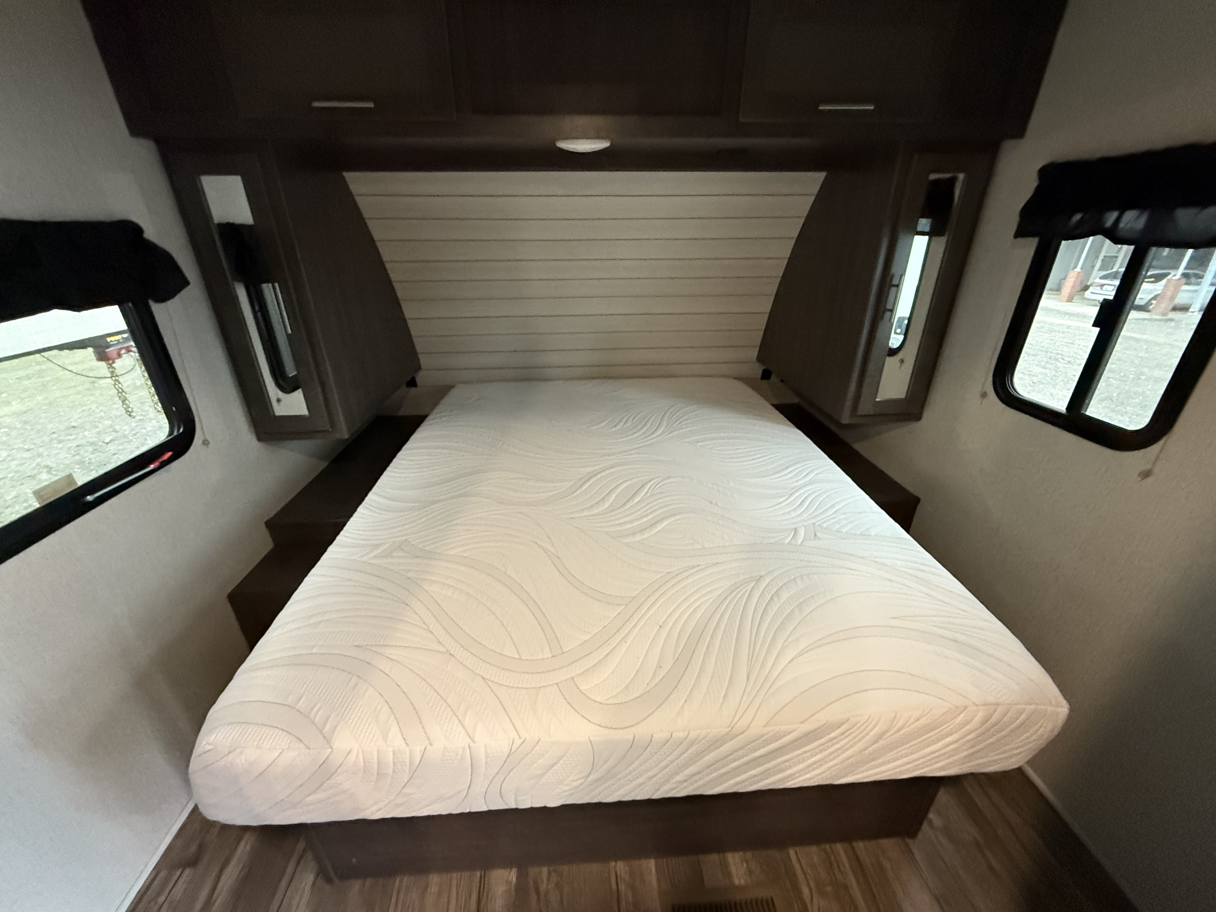 Comfortable RV rental bedroom featuring a large white mattress, dark wood storage, and side windows with outdoor views.. Crossroads Sunset Trail Super Lite 2019
