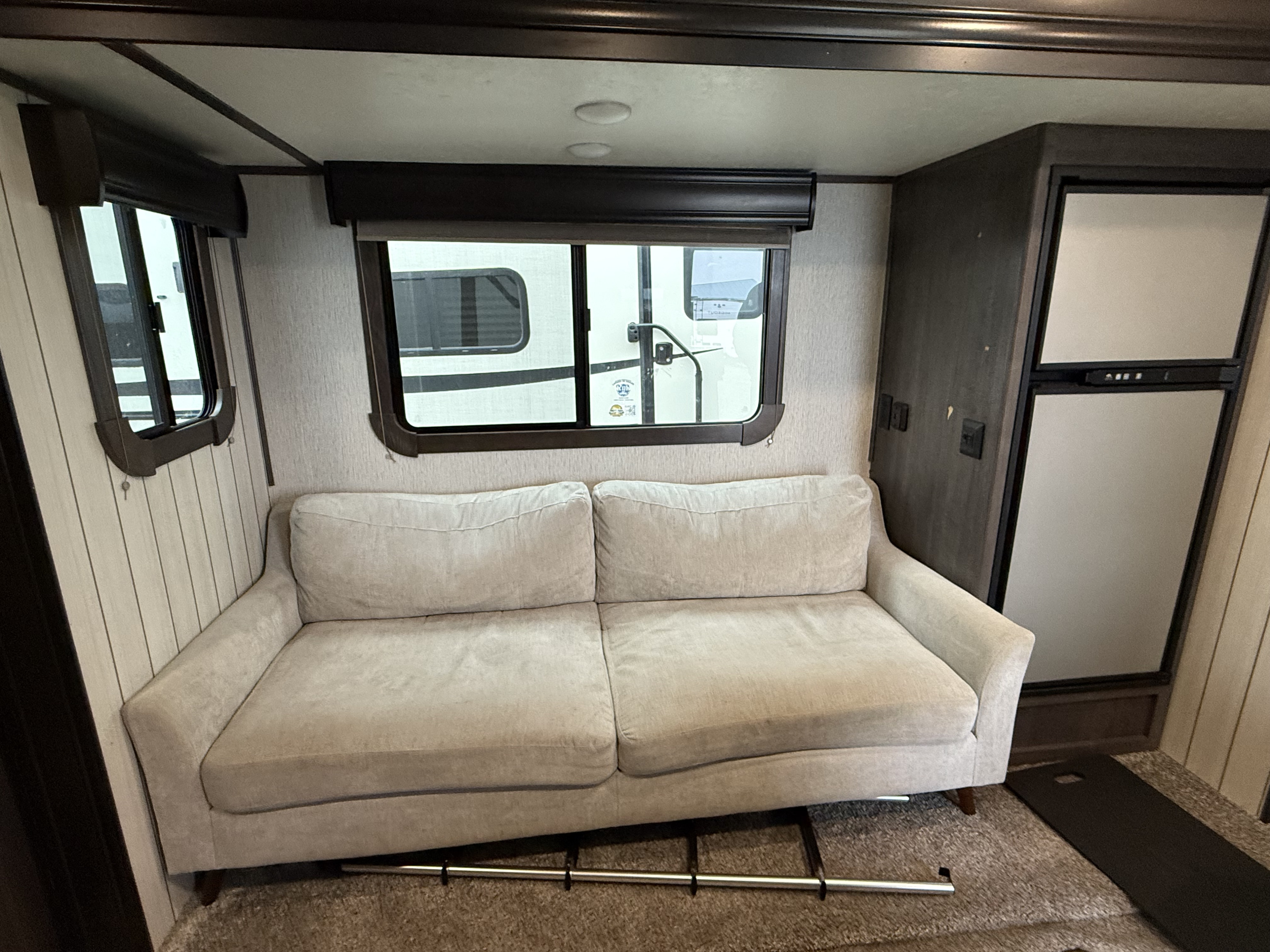 RV rental interior: A light two-seater sofa anchors the living area with large windows and a compact fridge on the right.. Crossroads Sunset Trail Super Lite 2019