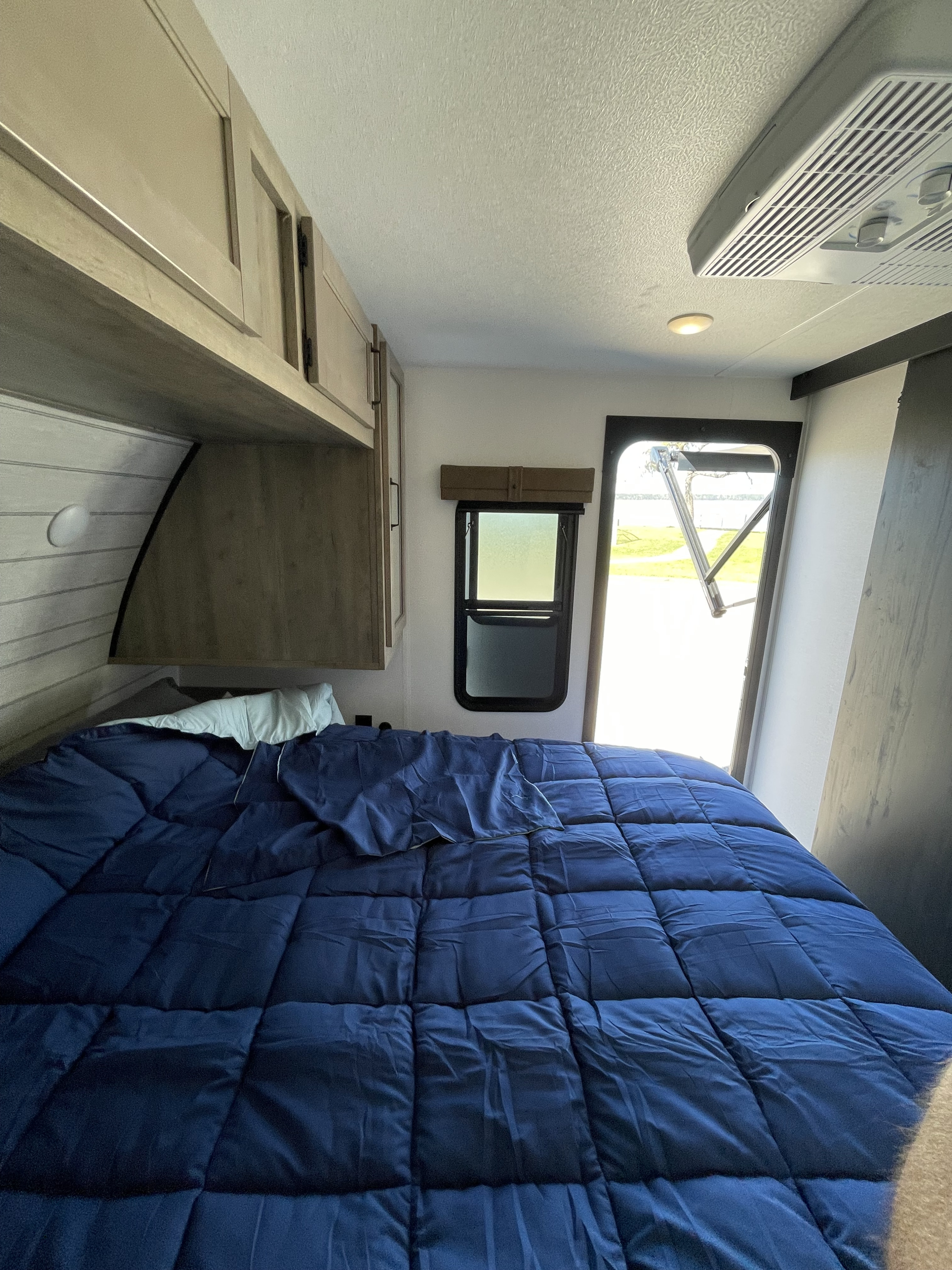 Cozy RV rental bedroom featuring a comfortable bed with blue bedding, overhead cabinets, and a bright view through the open door.. Palomino Puma 337BH 2025