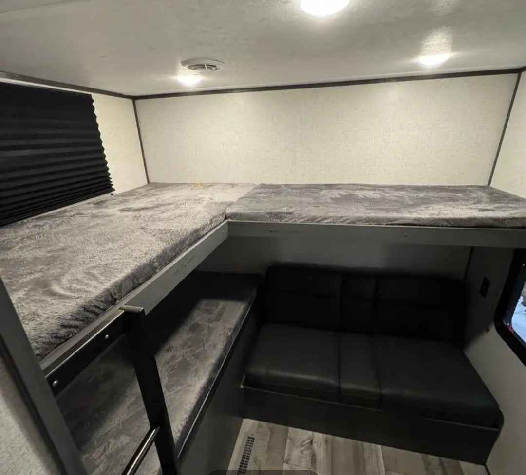 This RV rental features a modern interior with L-shaped bunk beds, a comfortable black sofa, and wood-look flooring.. Aspen Trail 3280BHS 2022
