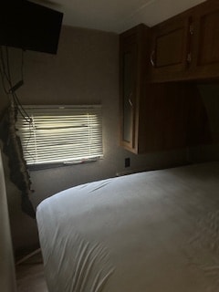 RV rental bedroom: a cozy interior with a comfortable bed, window with blinds, and wall-mounted TV, ideal for travel.. Coachmen 323TSQB 2016