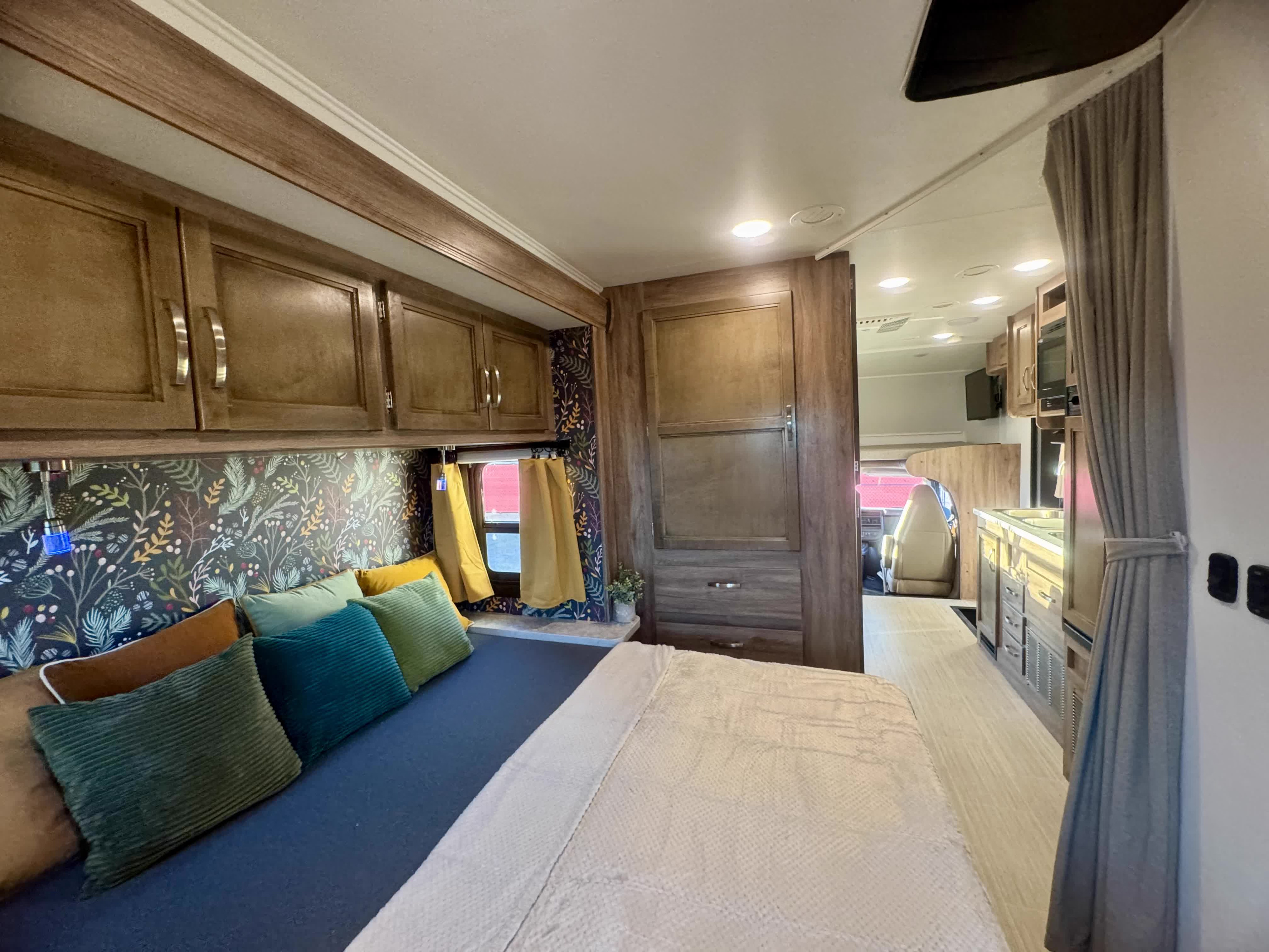 Inside a stylish RV rental, featuring a comfortable bedroom with patterned wallpaper and wood cabinets, open to a modern kitchen.. Jayco Redhawk 2021