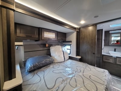 Spacious RV rental bedroom featuring a comfy bed, overhead storage, and a modern attached bathroom with a sink and mirror.. Forest River Coachmen Sportscoach SRS 2023