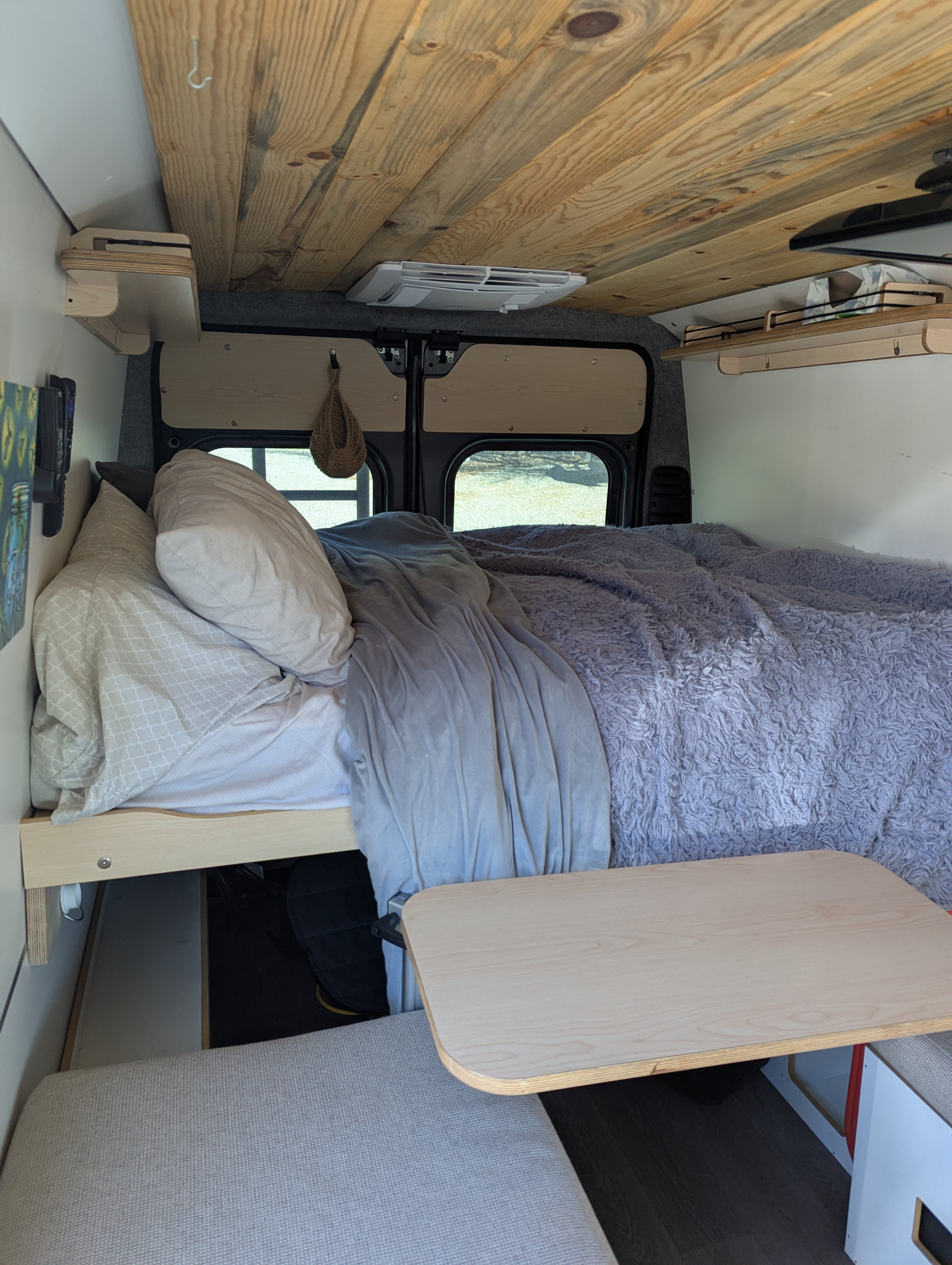 Inside an RV rental: a neatly made bed, wood-paneled ceiling with AC, and a light-colored table for comfort.. Dave & Matt Vans Dave & Matt Vans Class B 2024
