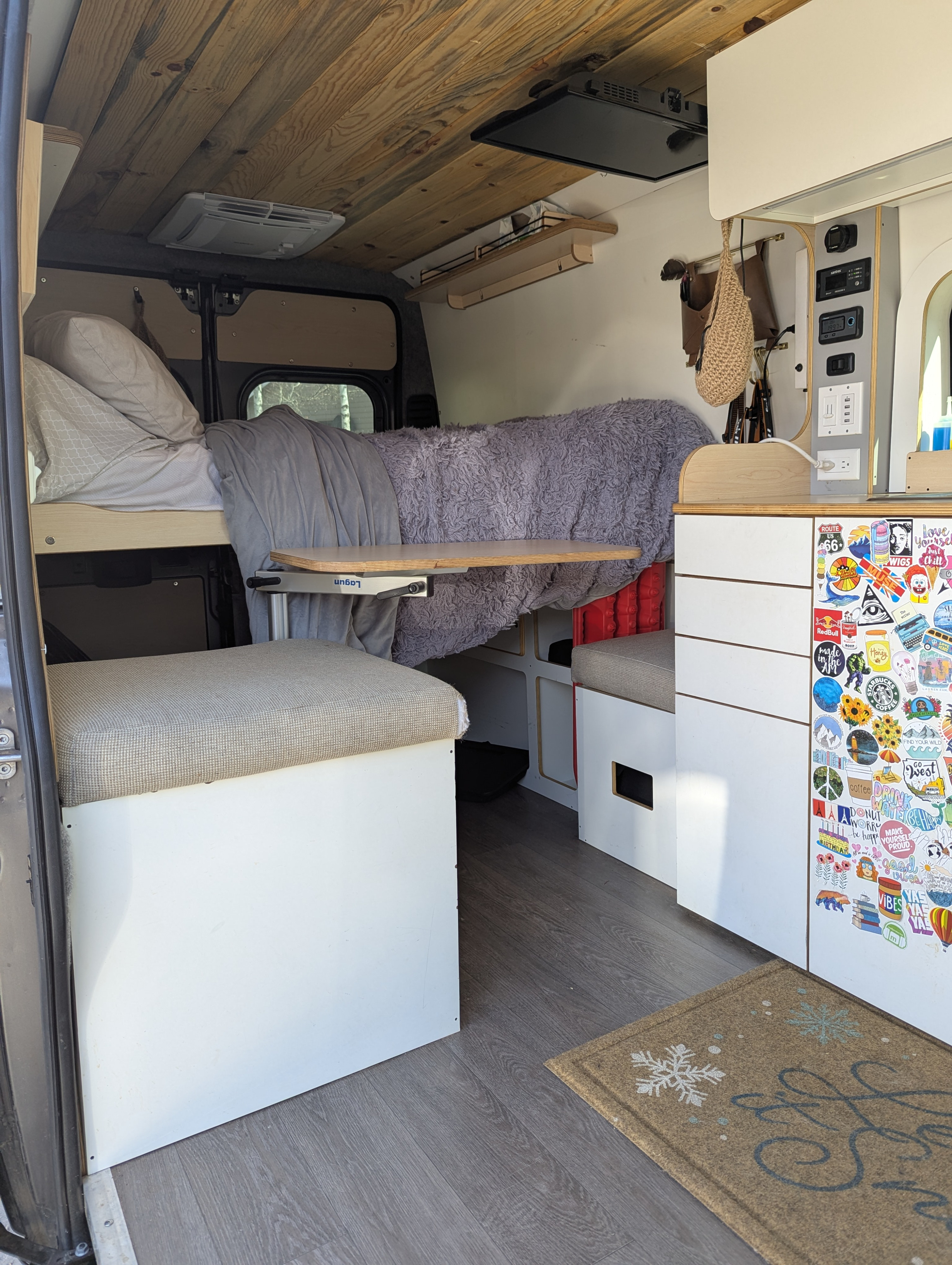 RV rental interior: wood ceiling, bed, adjustable table, control panel, and sticker-adorned storage for a cozy, functional space.. Dave & Matt Vans Dave & Matt Vans Class B 2024