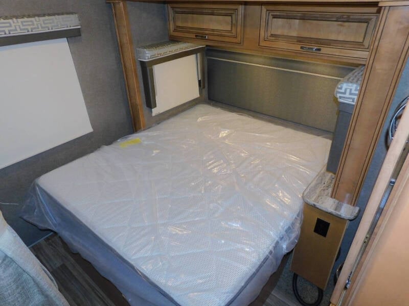 Inside this RV rental, a compact bedroom features a new, plastic-wrapped mattress, overhead storage, and window blind.. Thor Quantum 2017