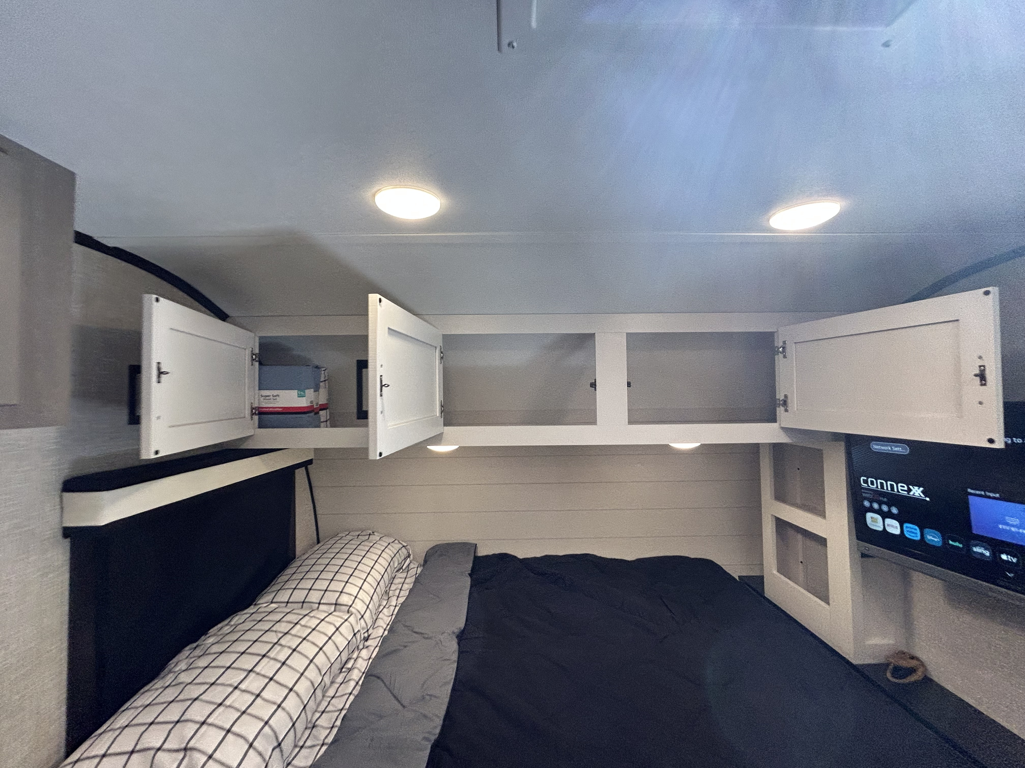 RV rental bedroom with practical overhead cabinets, a mounted TV, and a comfortable bed with checkered pillows.. Jayco Jay Feather Micro 2023
