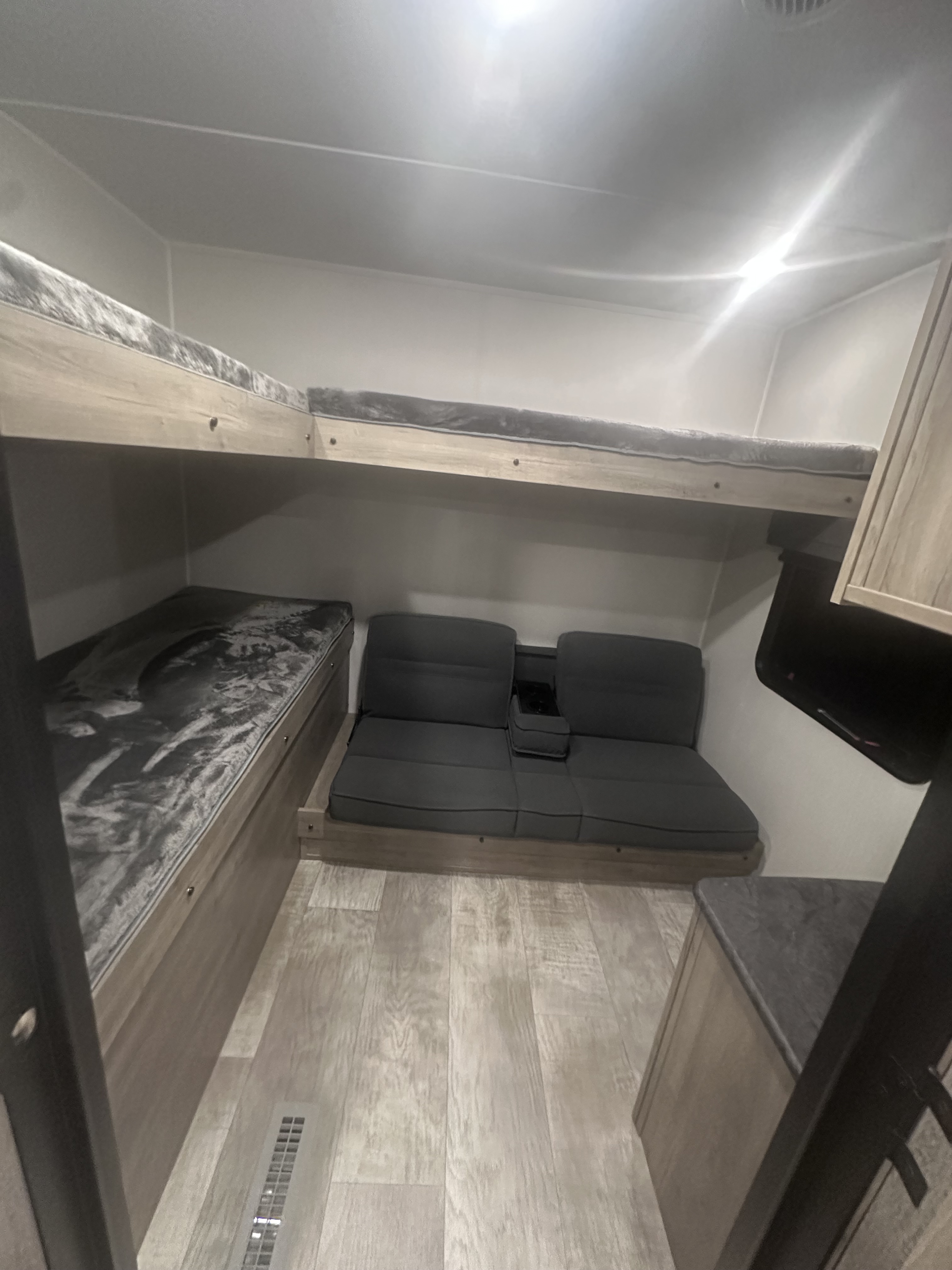 RV rental interior featuring modern bunk beds with grey bedding, a comfy sofa/dinette, and light wood-look flooring.. PALOMINO 28BHSS 2024