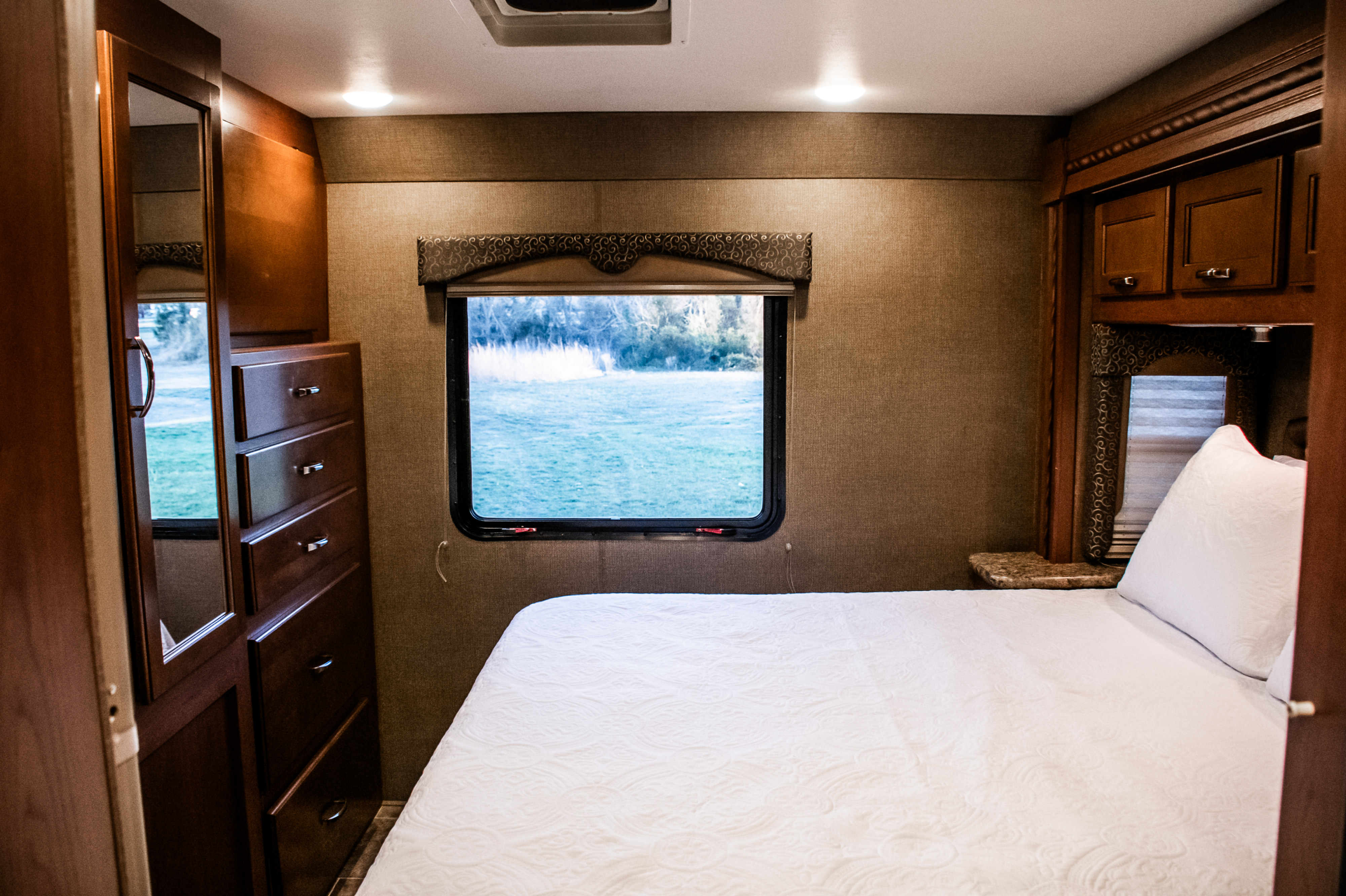 Cozy RV rental bedroom featuring a comfortable bed, wood storage, and a window offering a scenic outdoor view.. Thor Freedom Elite 2016