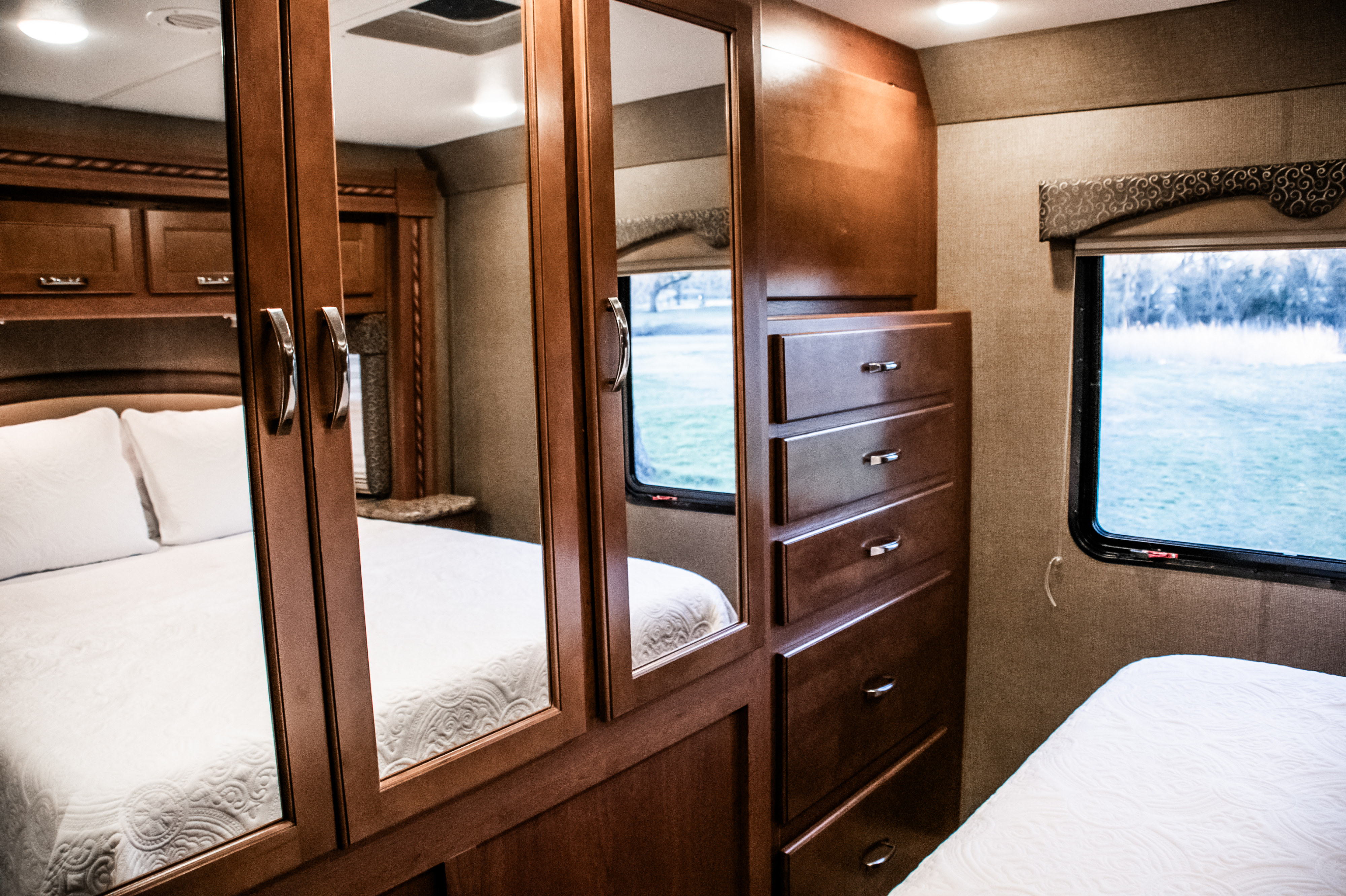Comfortable RV rental bedroom with mirrored closet, storage drawers, and a window offering outdoor views.. Thor Freedom Elite 2016