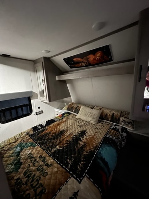Explore in comfort! Cozy RV rental bedroom with Bigfoot art, nature quilt, and "Home" pillow awaits your road trip.. Coachmen 2022 Coleman Dutchmen Coleman Lantern 334BH 2022