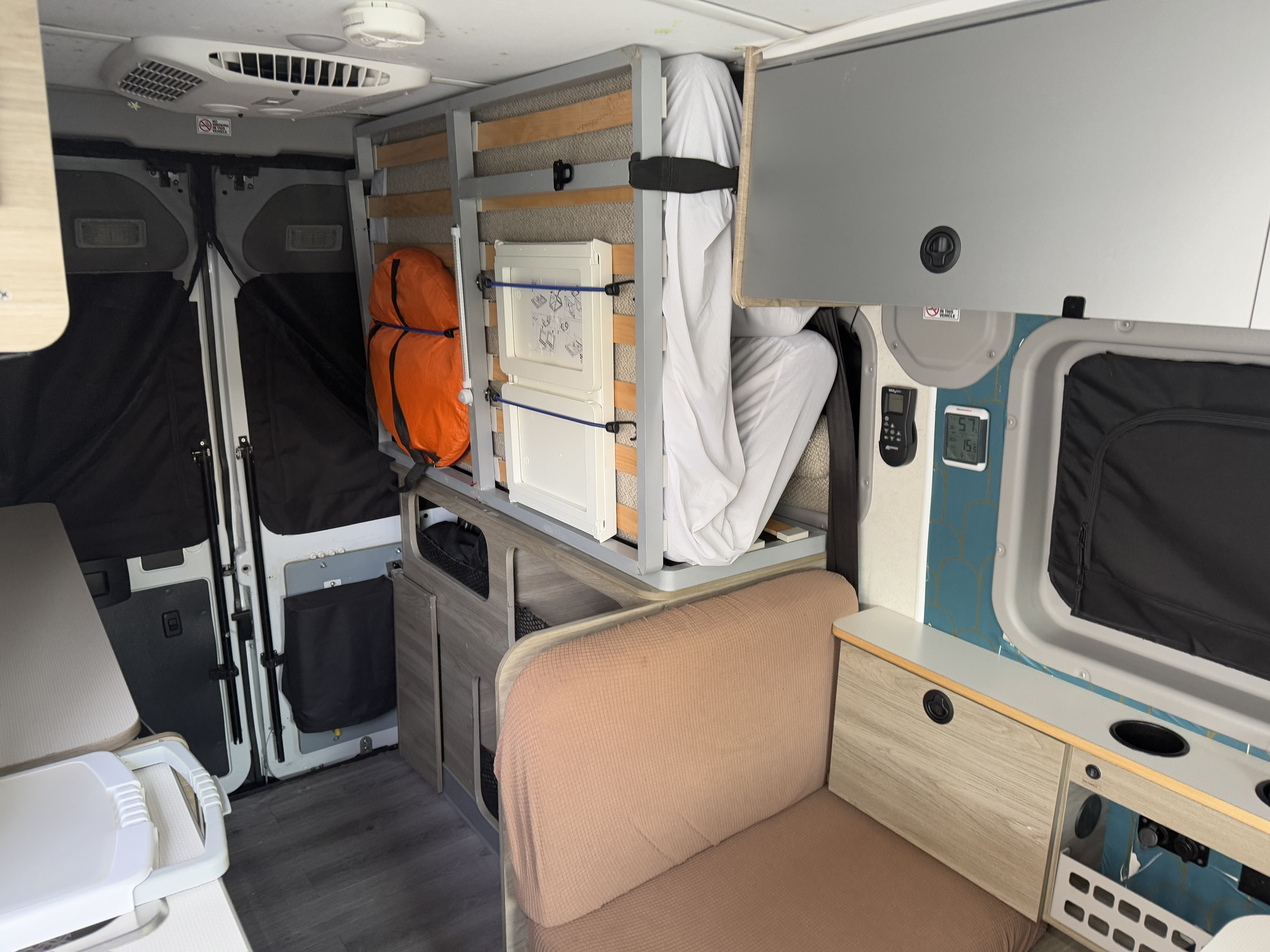 Compact RV rental interior showing a vertically folded bed, comfortable couch, and built-in storage solutions.. Winnebago Solis Pocket 2022