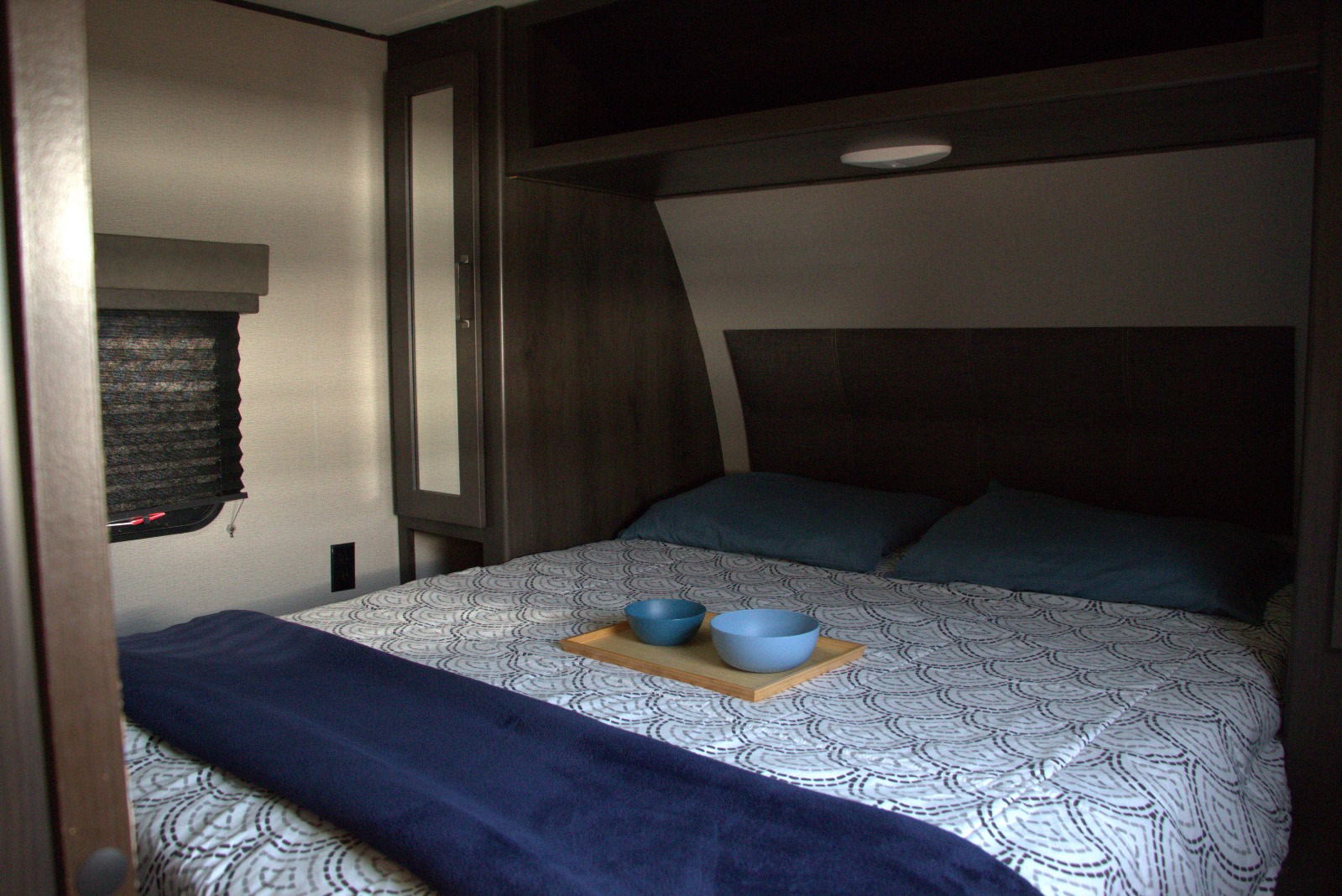 Cozy RV rental bedroom with a patterned duvet, teal pillows, and built-in storage. Ideal for comfortable travel.. Grand Design Transcend Xplor 2021