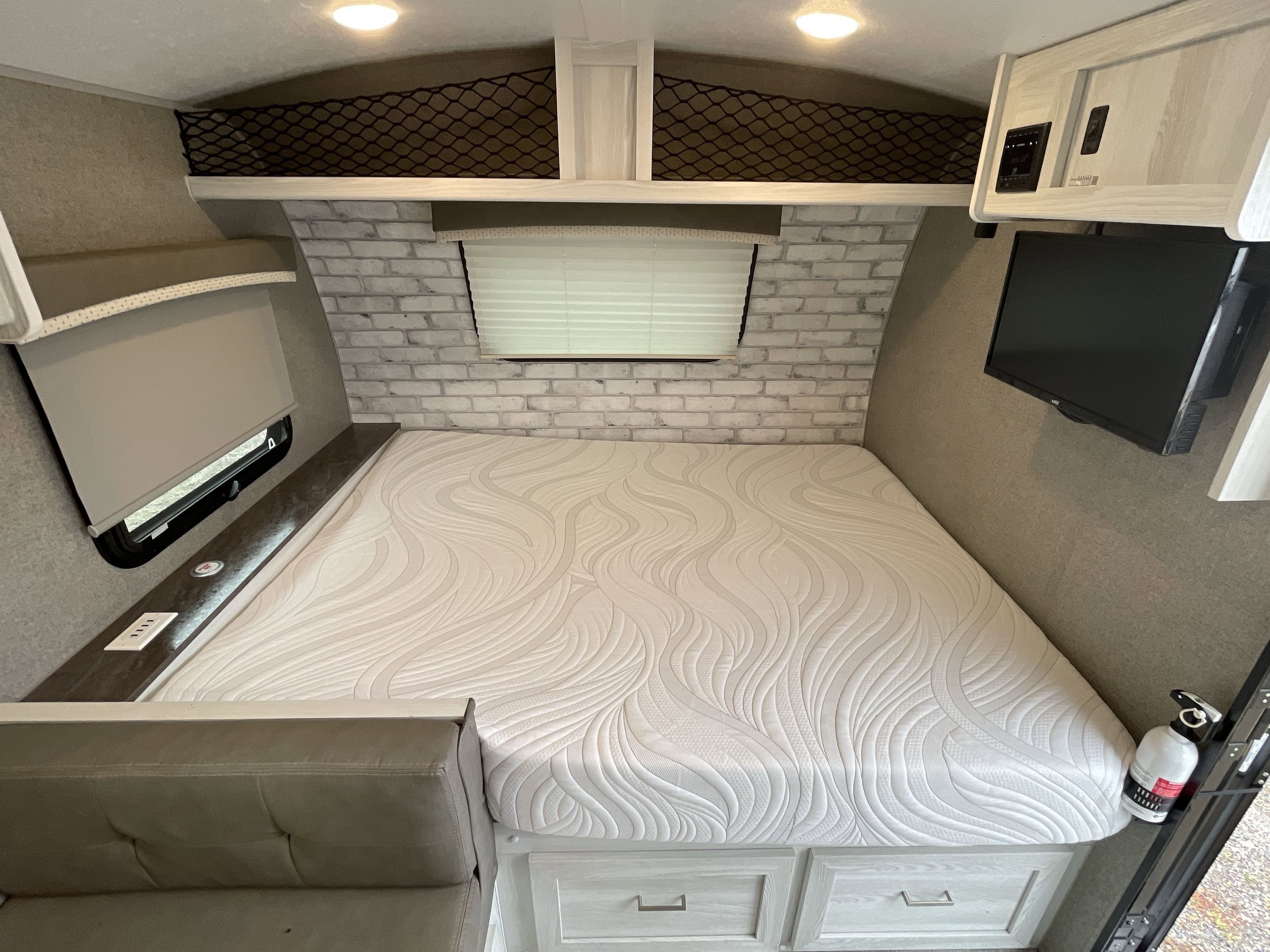 RV rental bedroom: spacious bed with textured mattress, overhead storage, TV, and a cozy seating area.. Forest River Rockwood Geo Pro 2022