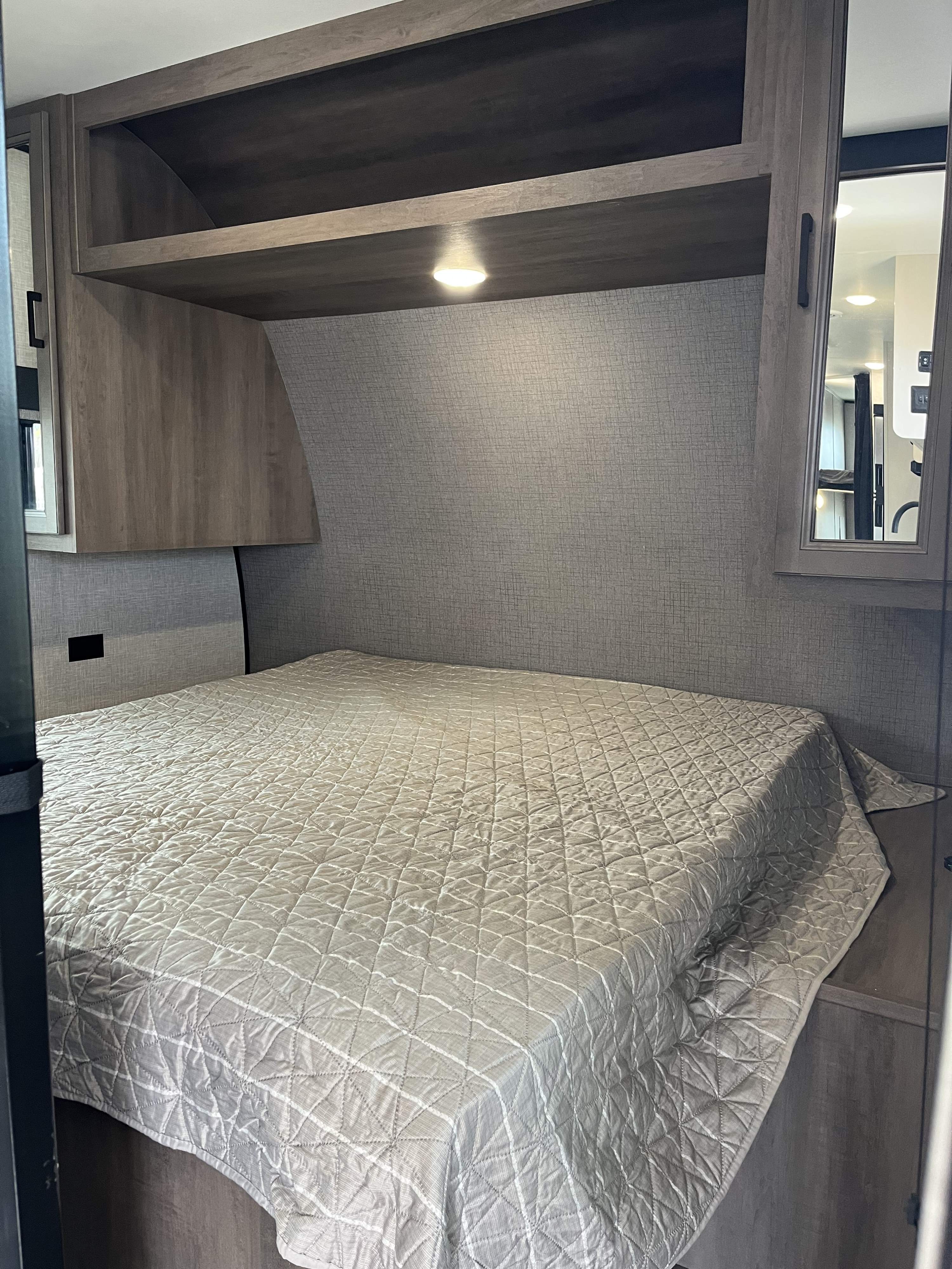 Cozy RV rental bedroom featuring a comfortable bed with quilted comforter, overhead storage, and built-in light.. Highland Ridge RV Go Play 2023