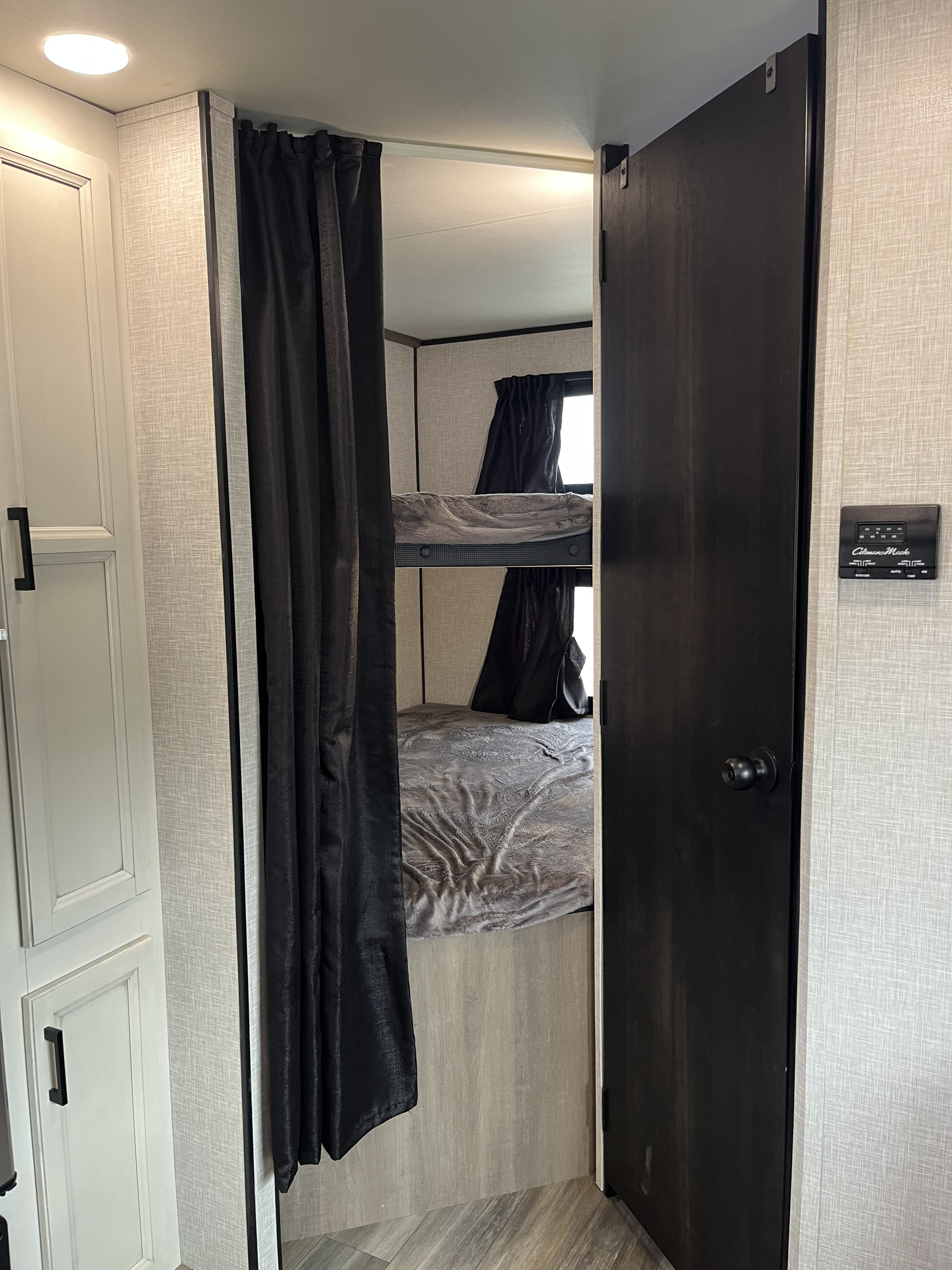 View of an RV rental interior featuring a bunk bed sleeping area with dark privacy curtains and an open door.. Highland Ridge RV Go Play 2023