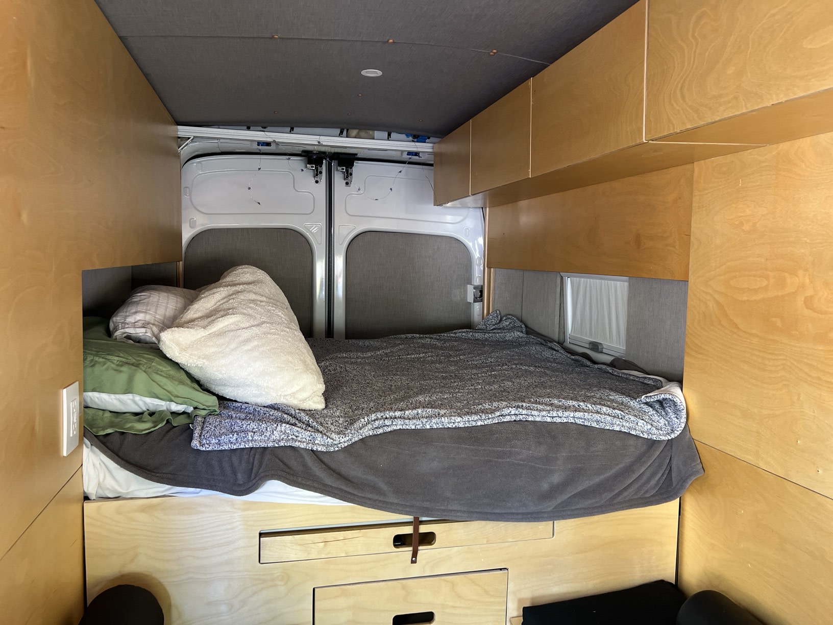 Explore this cozy RV rental's custom interior: a built-in bed with pillows, wooden cabinets, and rear doors.. Ford Custom Transit 2022