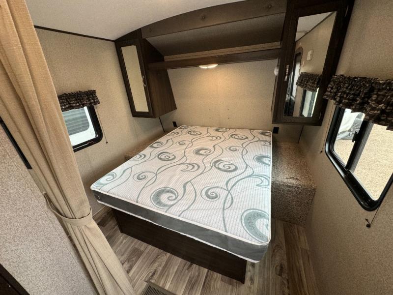 Cozy RV rental bedroom with a comfortable bed, overhead cabinets, windows, and wood-look flooring for your trip.. Keystone RV Springdale 2019