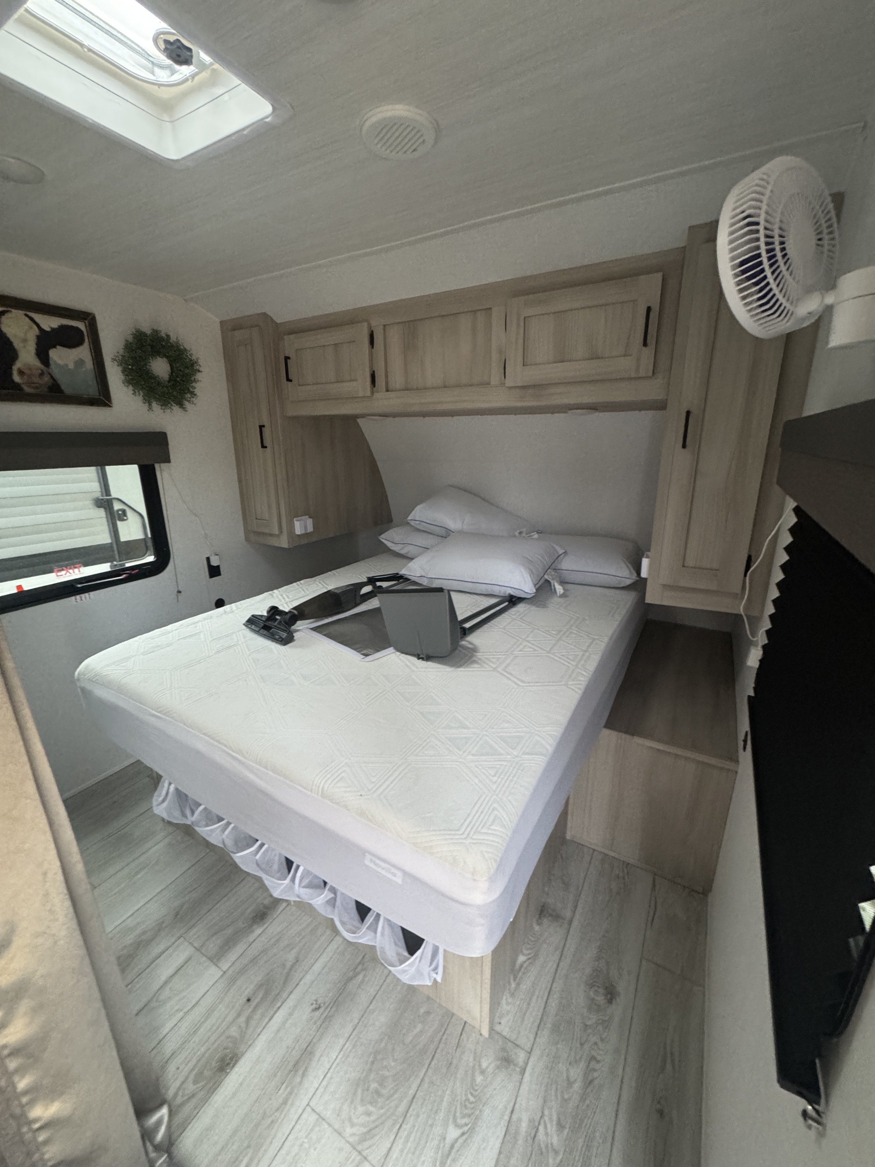 RV rental bedroom interior featuring a bed with white mattress & pillows, light wood cabinets, skylight, and wall-mounted fan.. East to West Silver Lake LE 2024